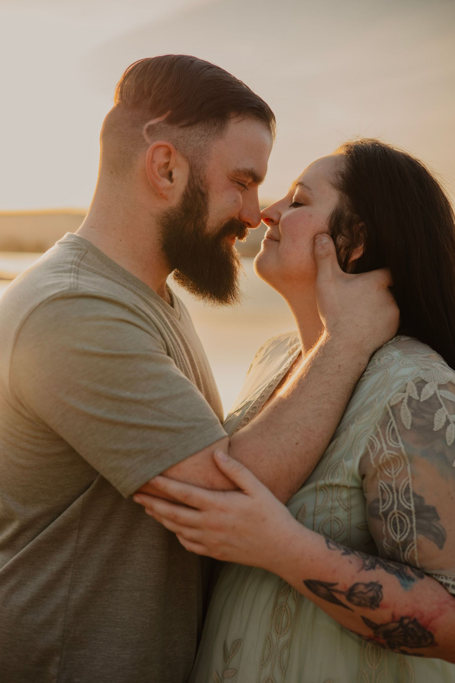 A tender close-up portrait of a couple touching noses in warm sunset light.