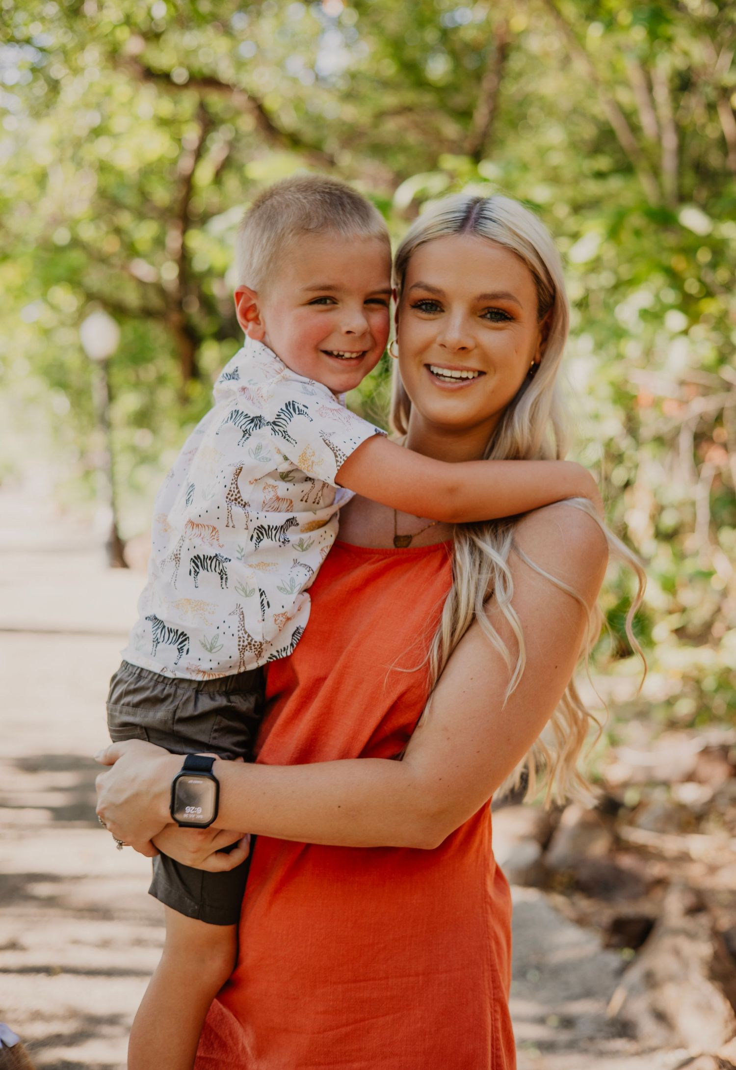 A heartwarming outdoor portrait of parent and child embracing on a sunny day with natural foliage in the background.