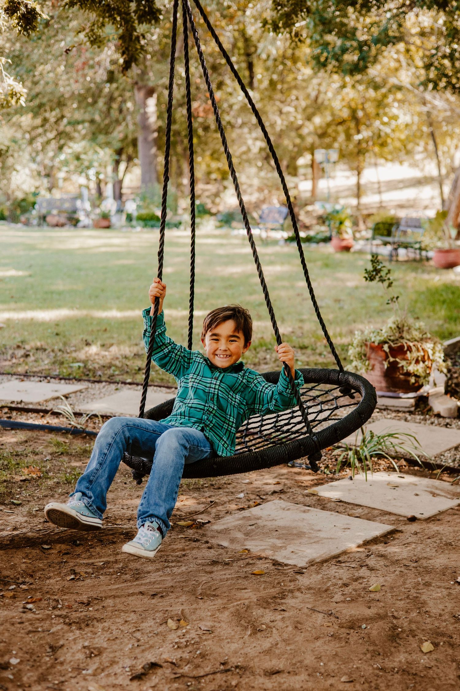 Child smiling while swinging on round nest swing in park setting.