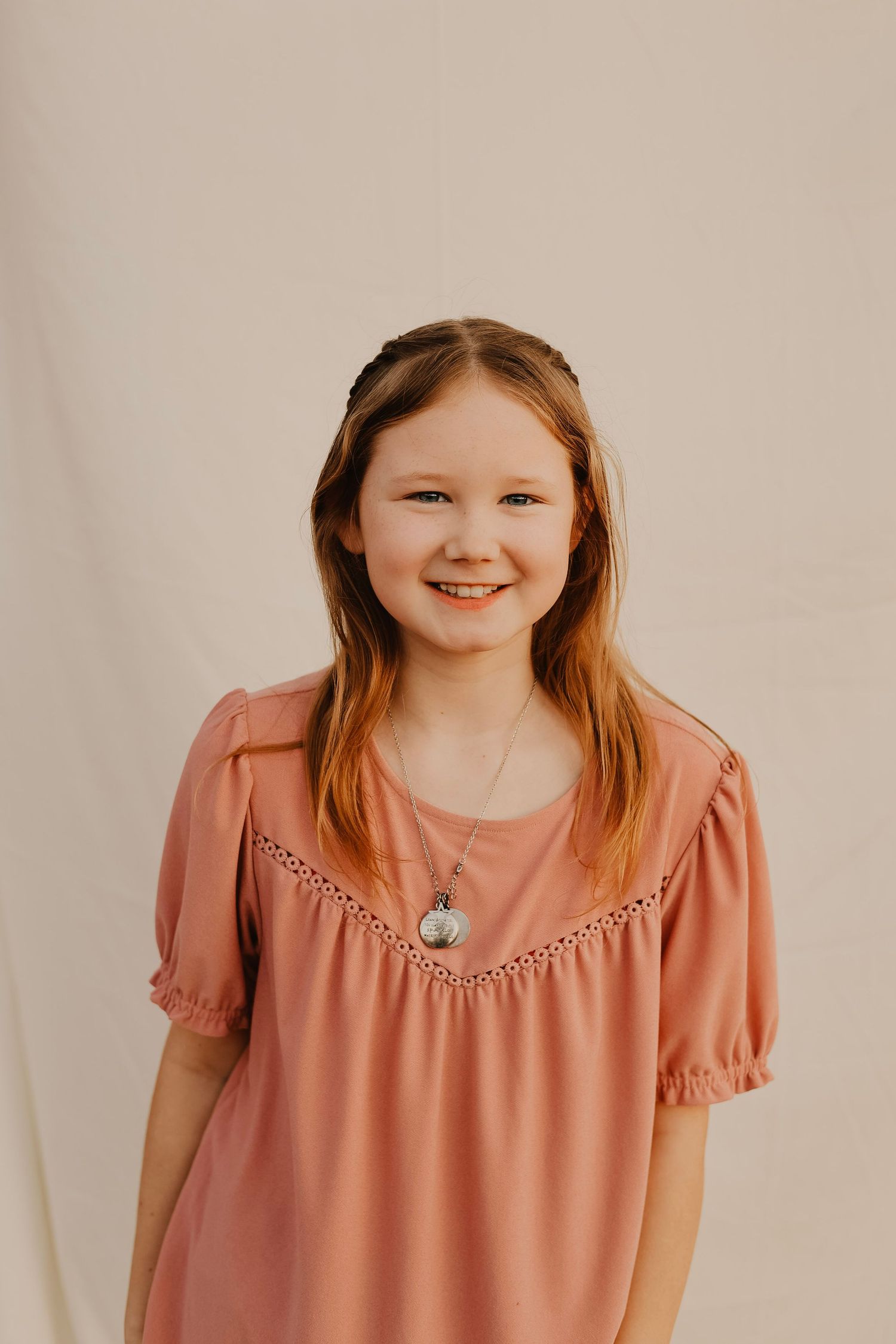 Studio portrait of person in coral colored blouse with lace detail against neutral background.