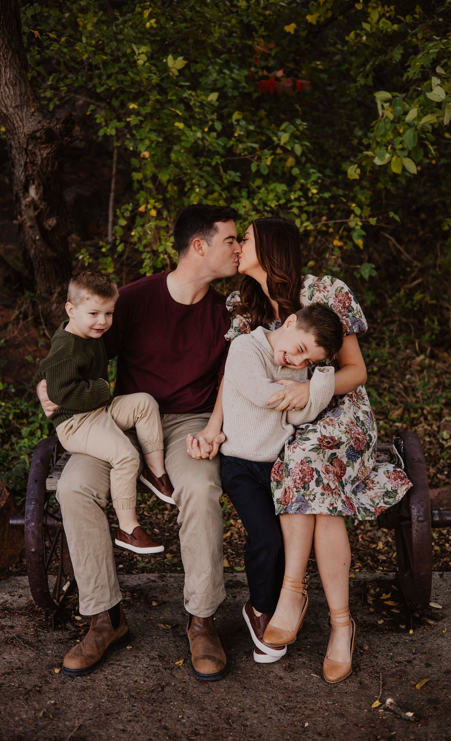 Family shares tender moment together on park bench surrounded by autumn foliage.