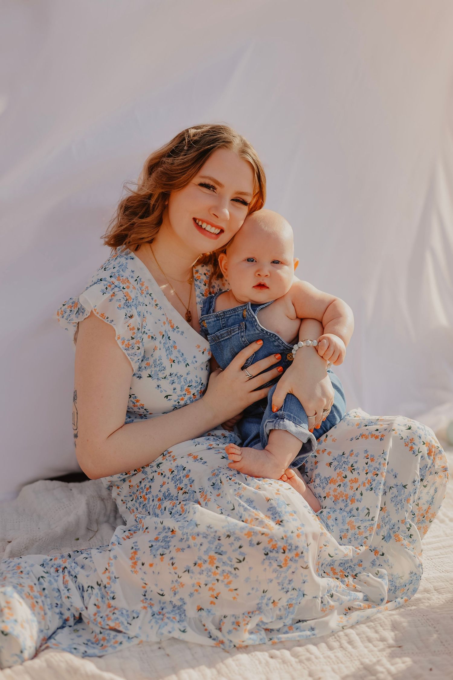 Joyful moments shared between parent and baby on white blanket with floral dress.