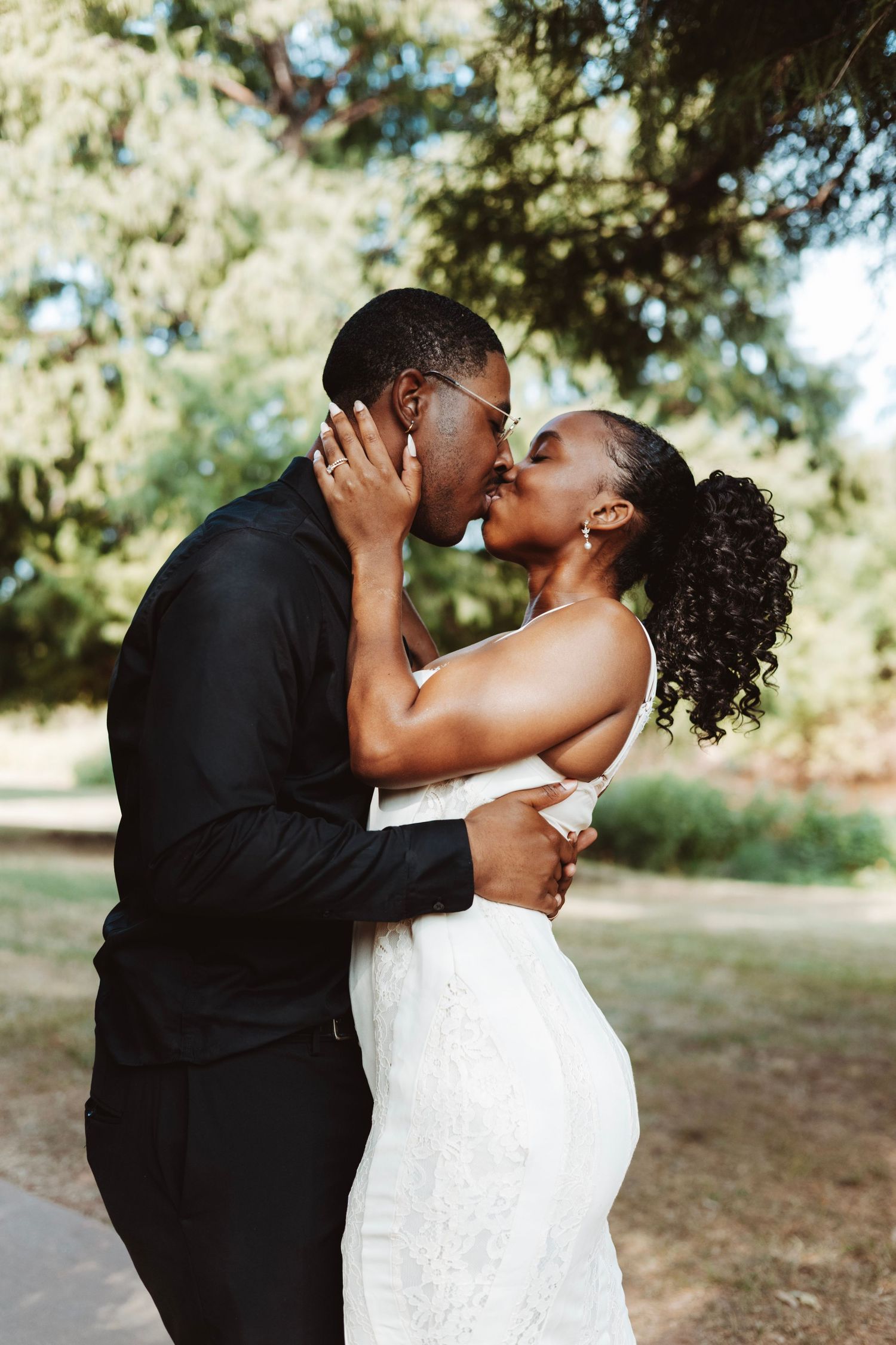 Bride and groom sharing a romantic outdoor kiss in formal wedding attire.