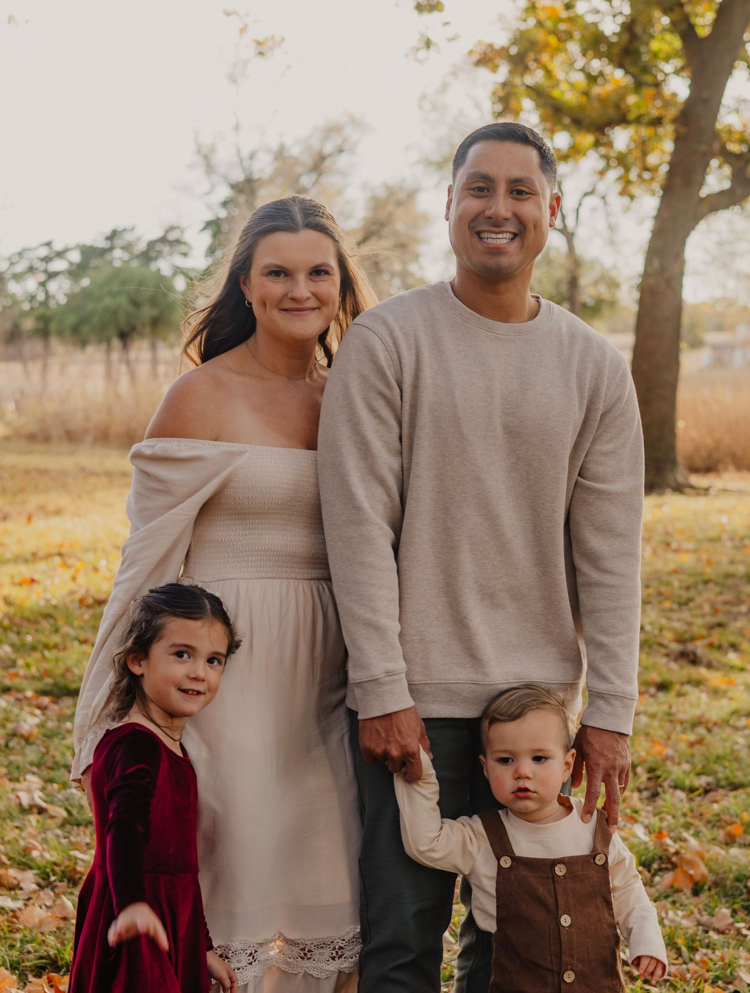Family of four posing together outdoors in coordinated neutral outfits.