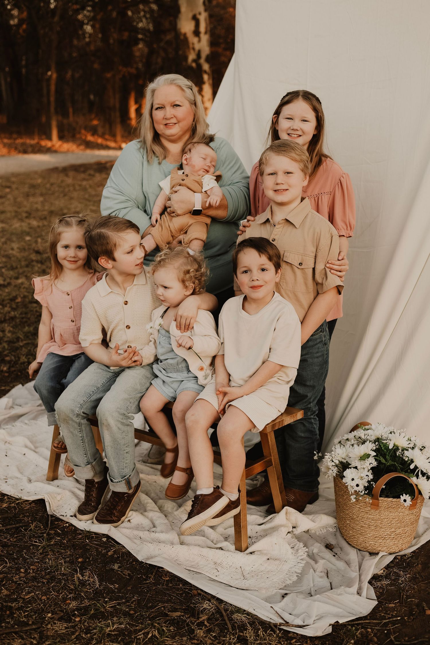 Multi-generational family portrait with children arranged on wooden stools against white backdrop.