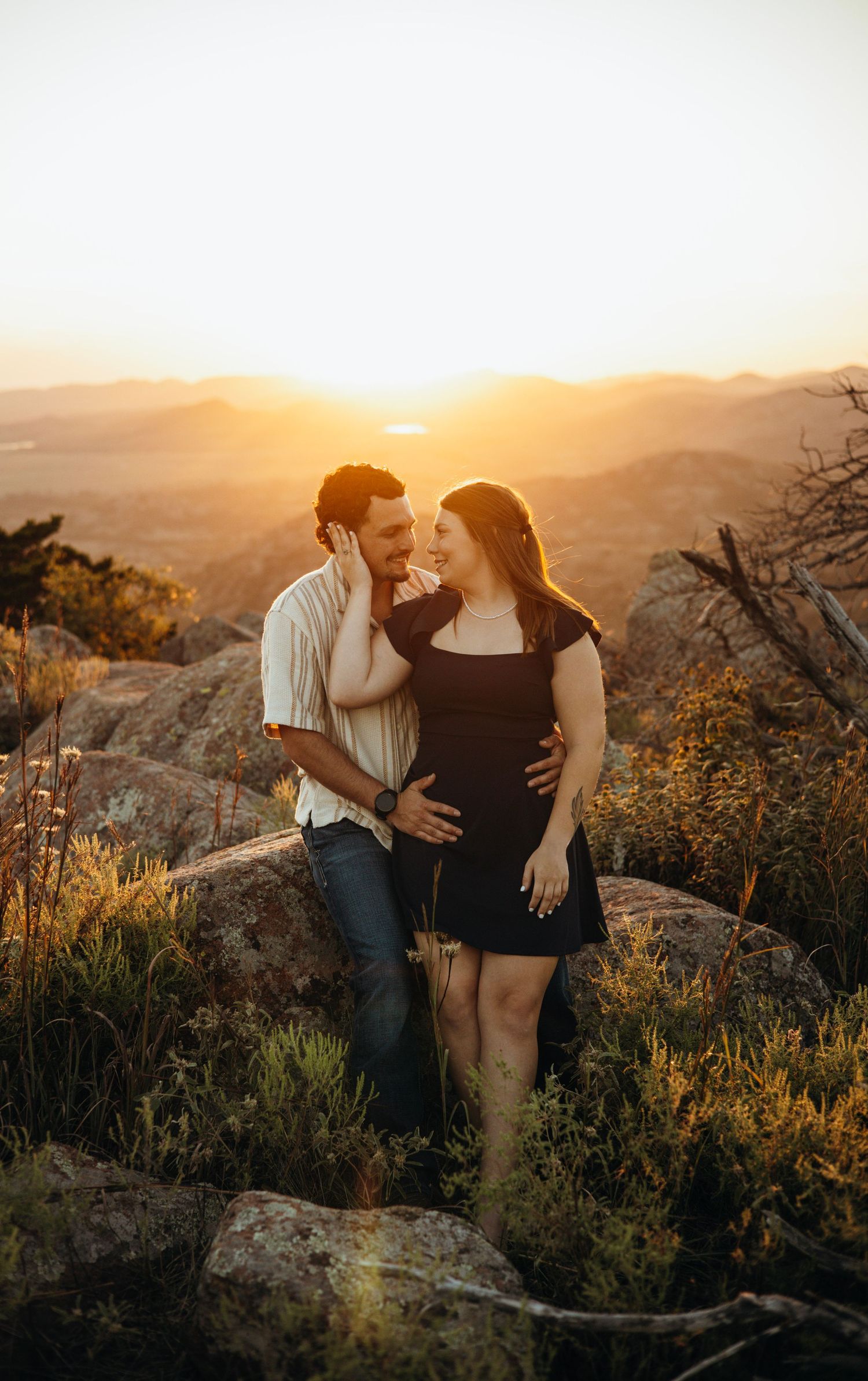 A couple enjoying a sunset moment together on a rocky mountain overlook.