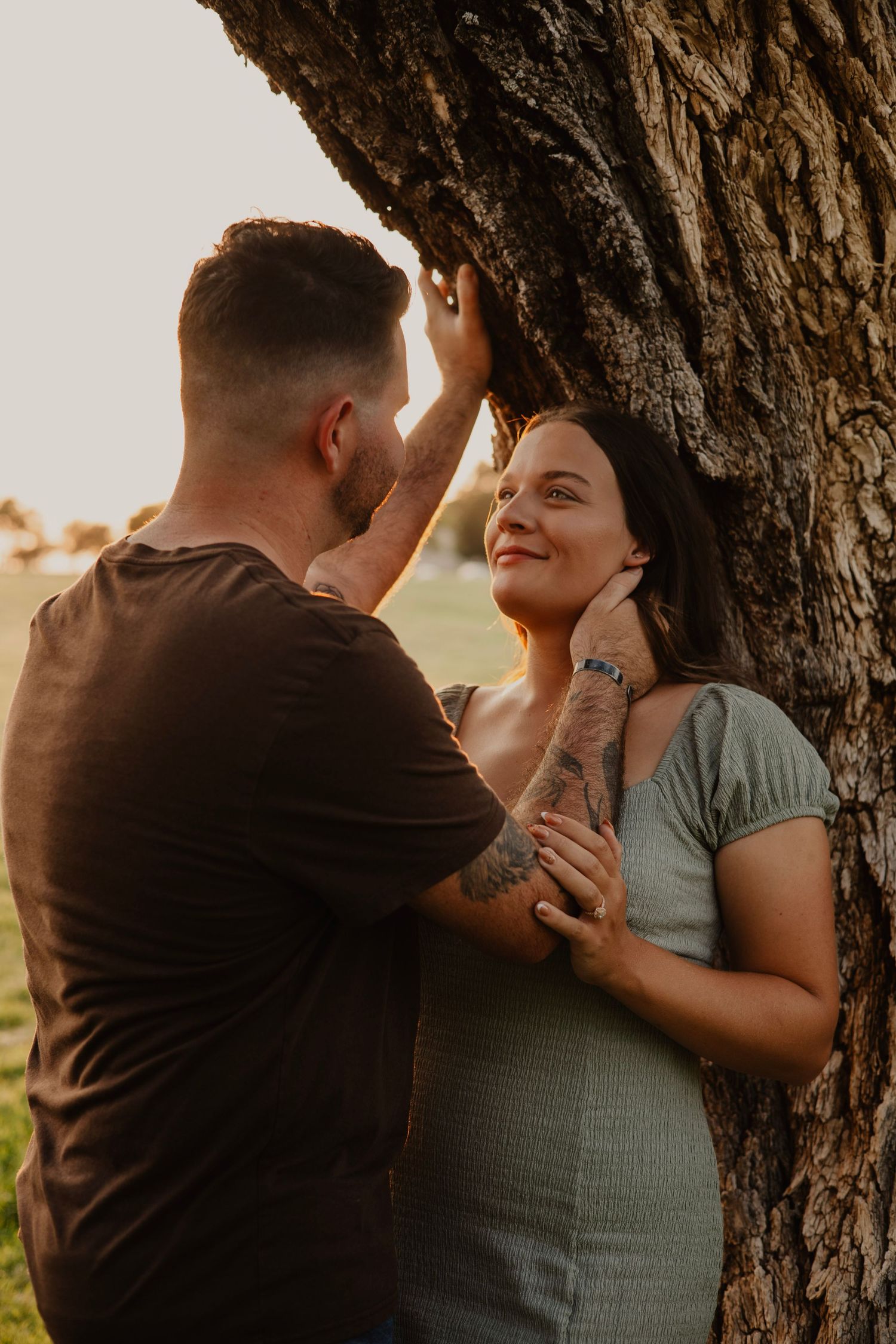 Romantic couple sharing an intimate moment under a large tree during golden hour.