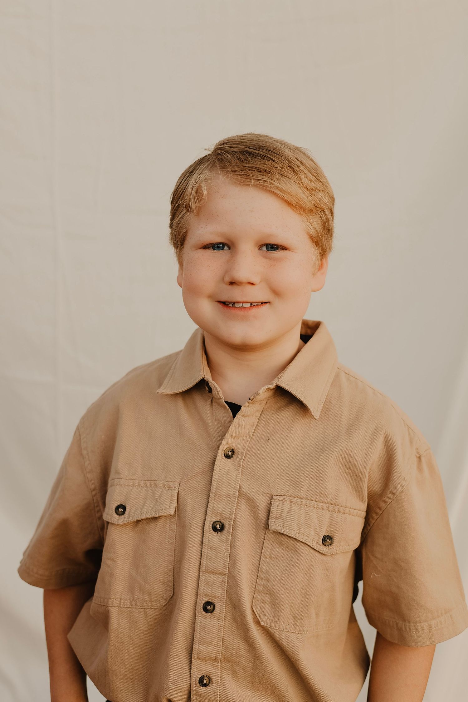 Studio portrait of person in tan button-up shirt against neutral background.