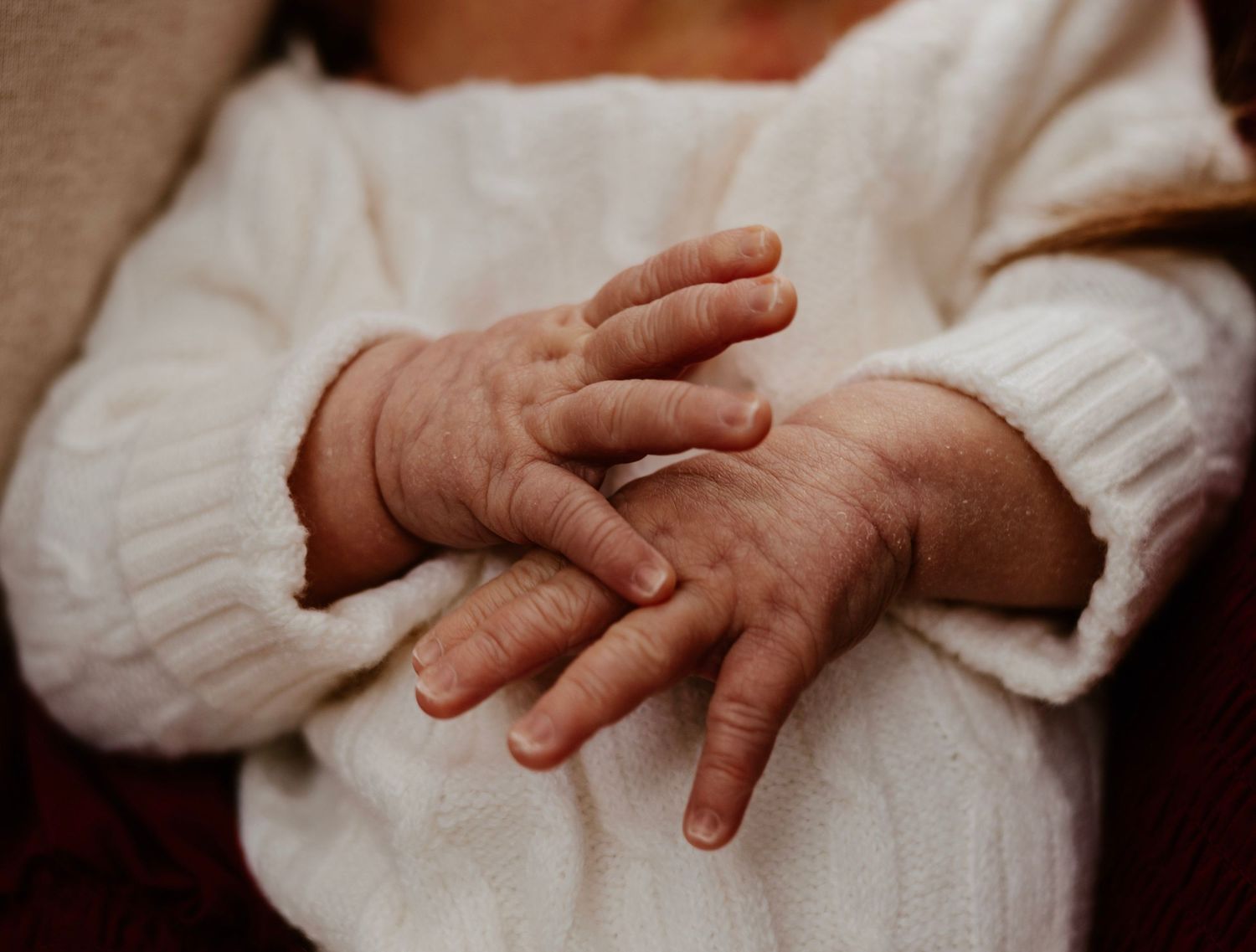 Artistic series of baby hands being tenderly held against white fabric.