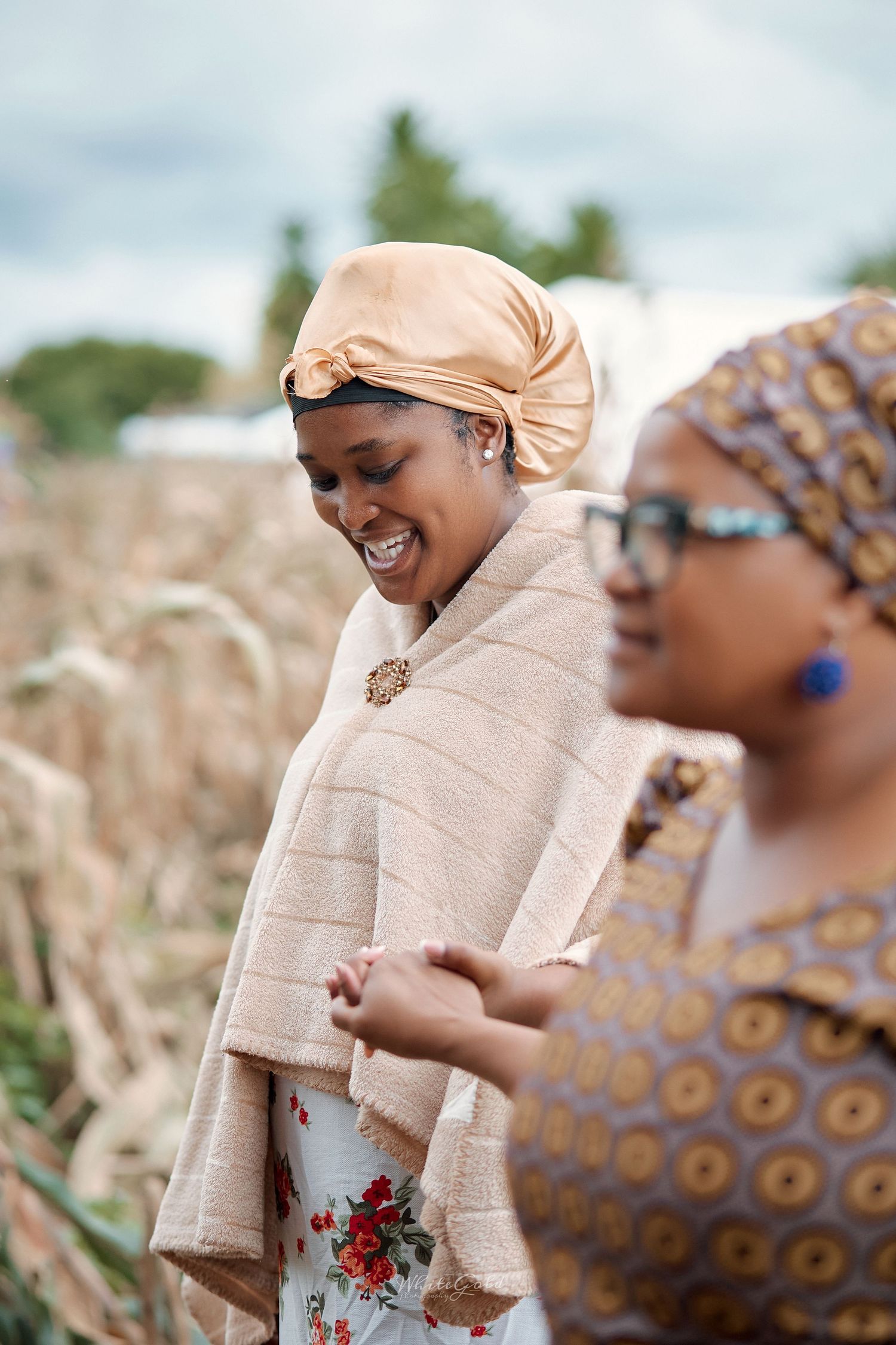 Smiling woman in golden headwrap and floral dress at outdoor cultural event.