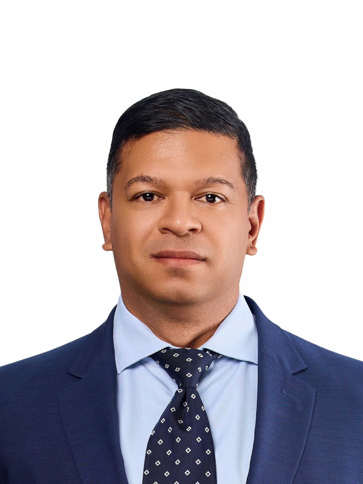 Professional headshot of a man in a navy blue suit and dotted tie against a white background.