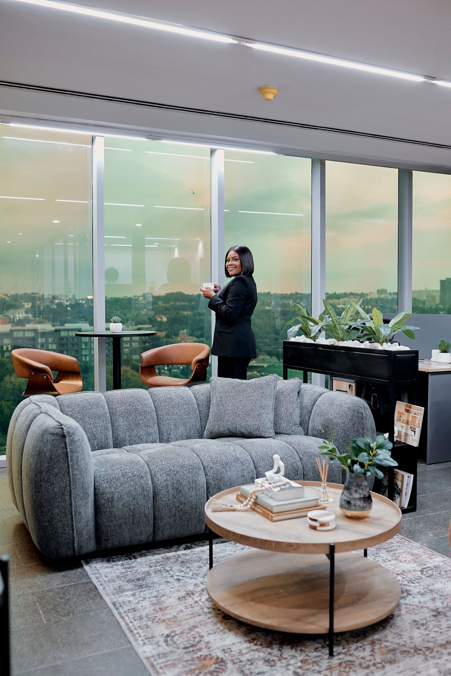 Professional Black woman in a black suit standing by large windows in a modern office lounge.