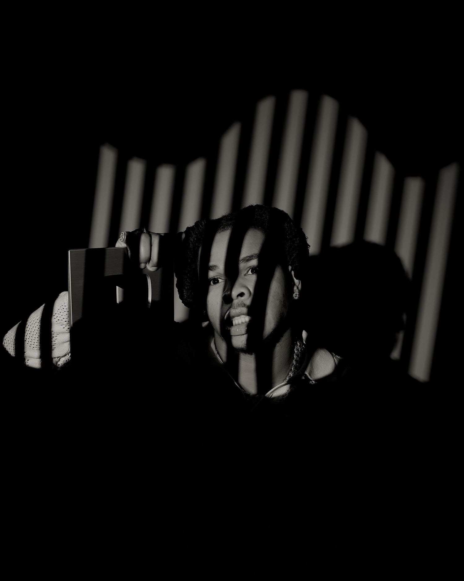 Black and white dramatic portrait of a person with striped shadow patterns across their face.