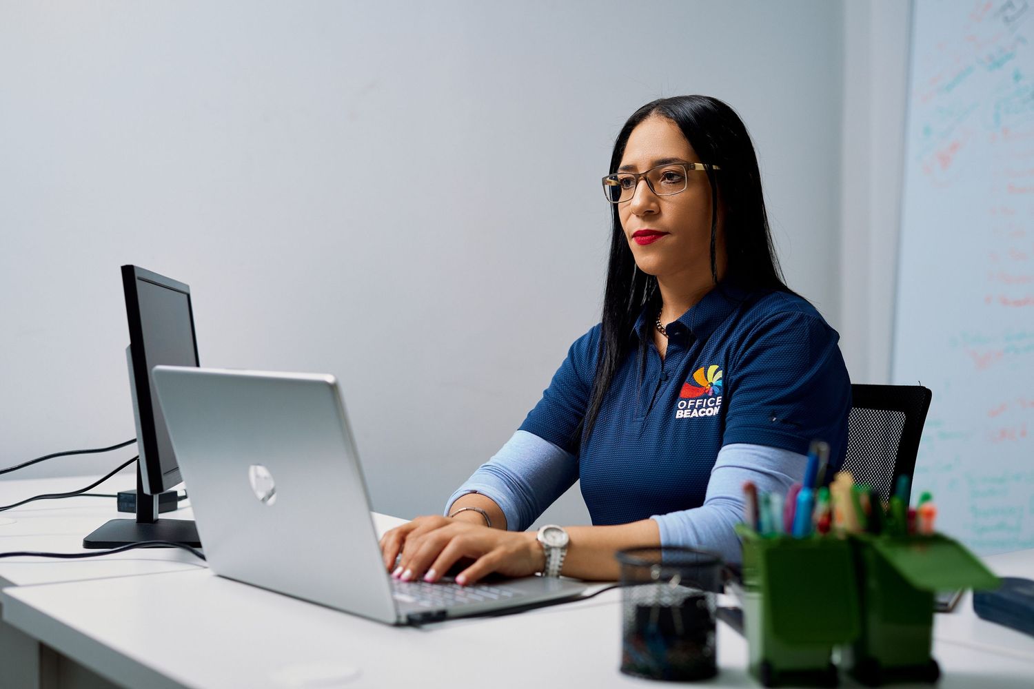 Professional woman in navy polo shirt working on a laptop at a clean office desk.