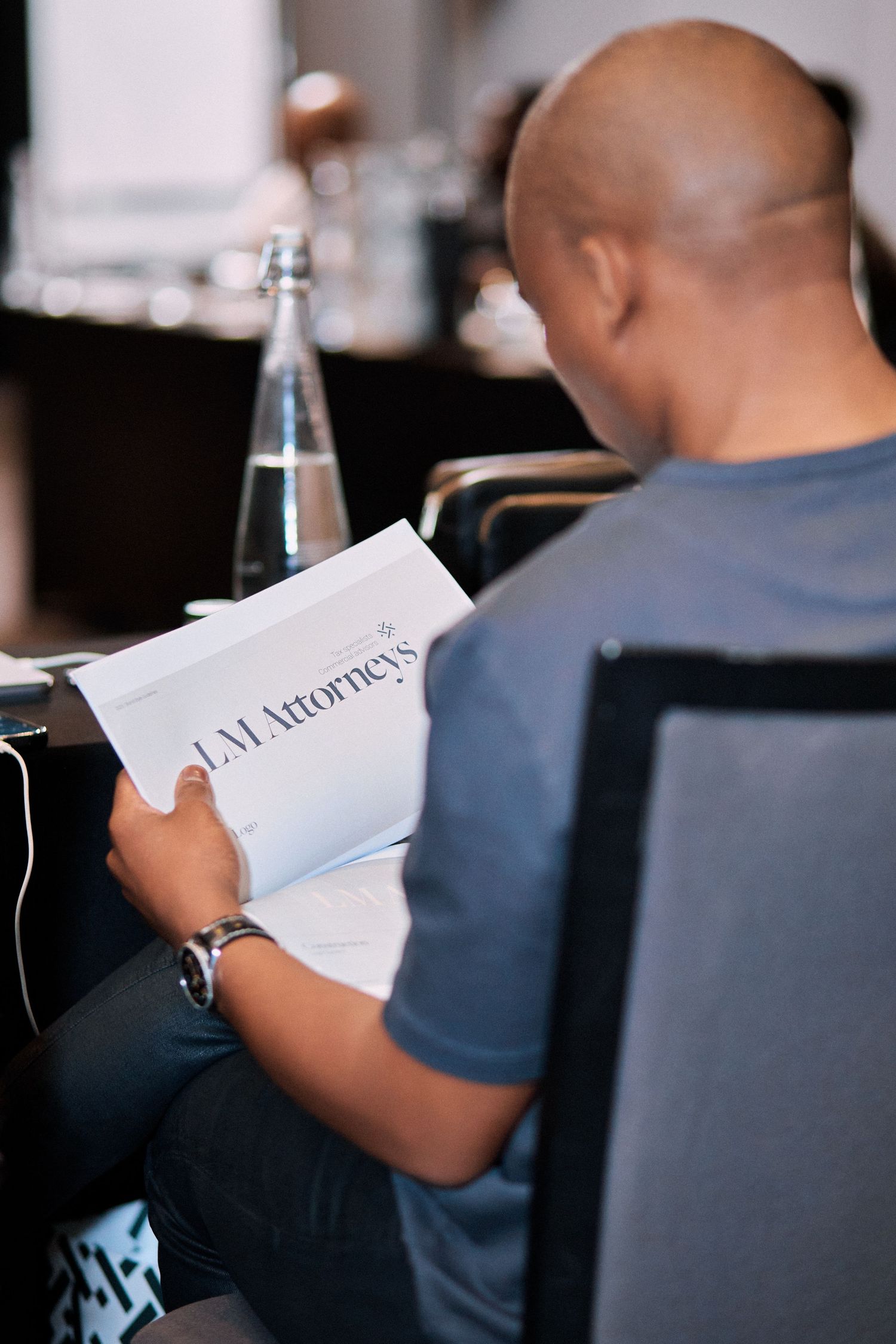 A man reads an LM Attorneys booklet while seated at a conference table with a water bottle nearby.