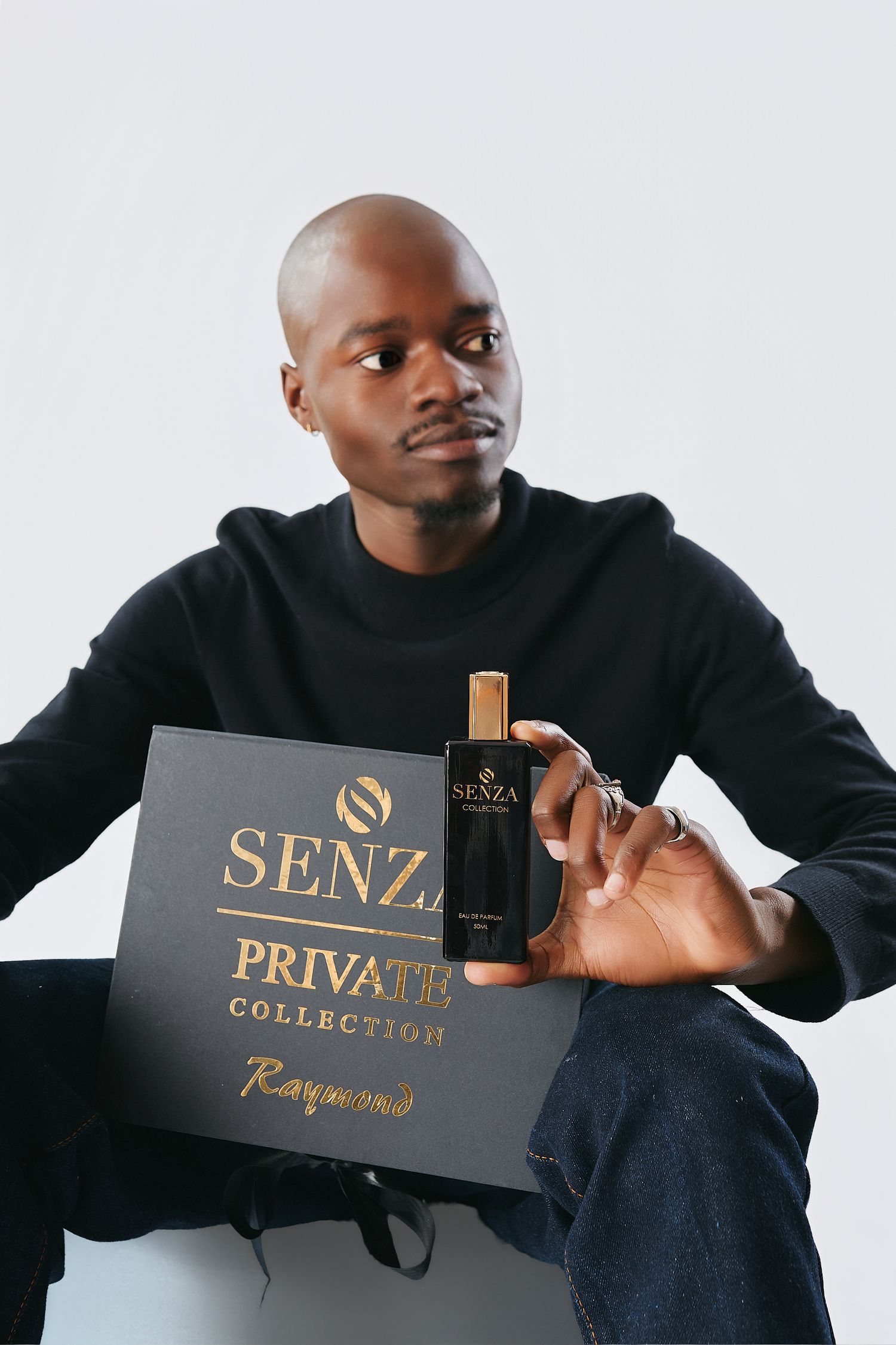 Bald man in black sweater posing with Senza Private Collection perfume and luxury gift box.