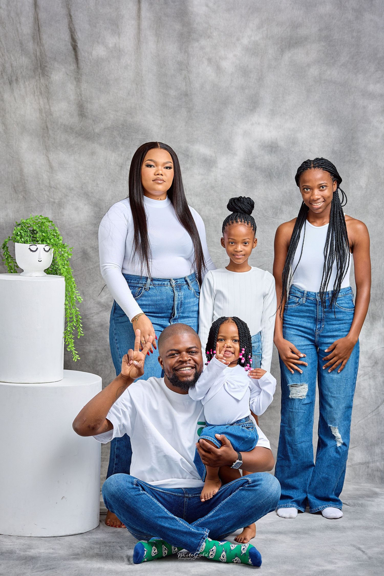 Happy Black family of five in matching white tops and jeans poses together in a studio setting.