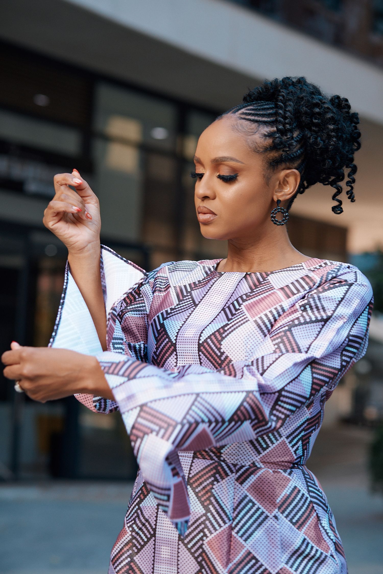 Woman adjusting sleeve of colorful geometric patterned long-sleeve dress outside modern building.
