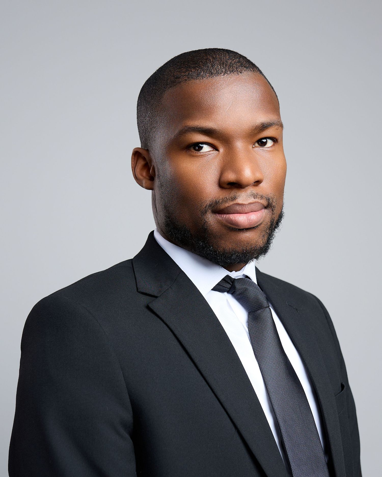 Young Black man in black suit and tie poses for sleek professional headshot portrait.