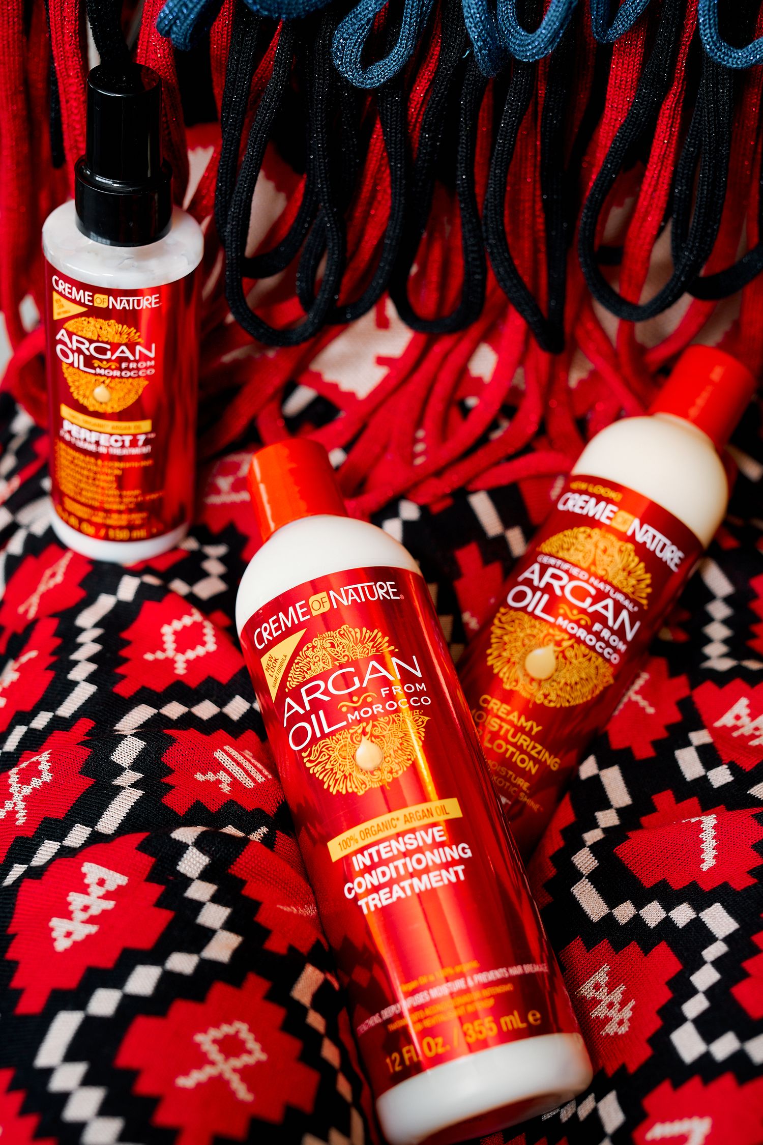 Creme of Nature Argan Oil hair care products including conditioner and treatment on patterned fabric.