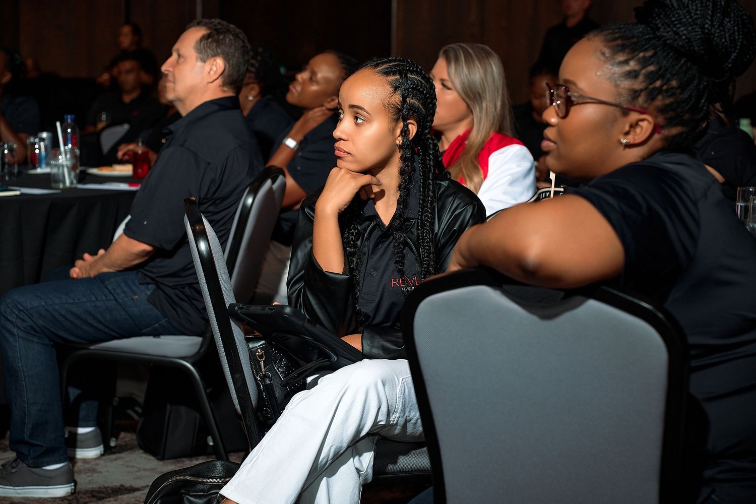 Attendees seated at round tables listen attentively during a professional conference or event.