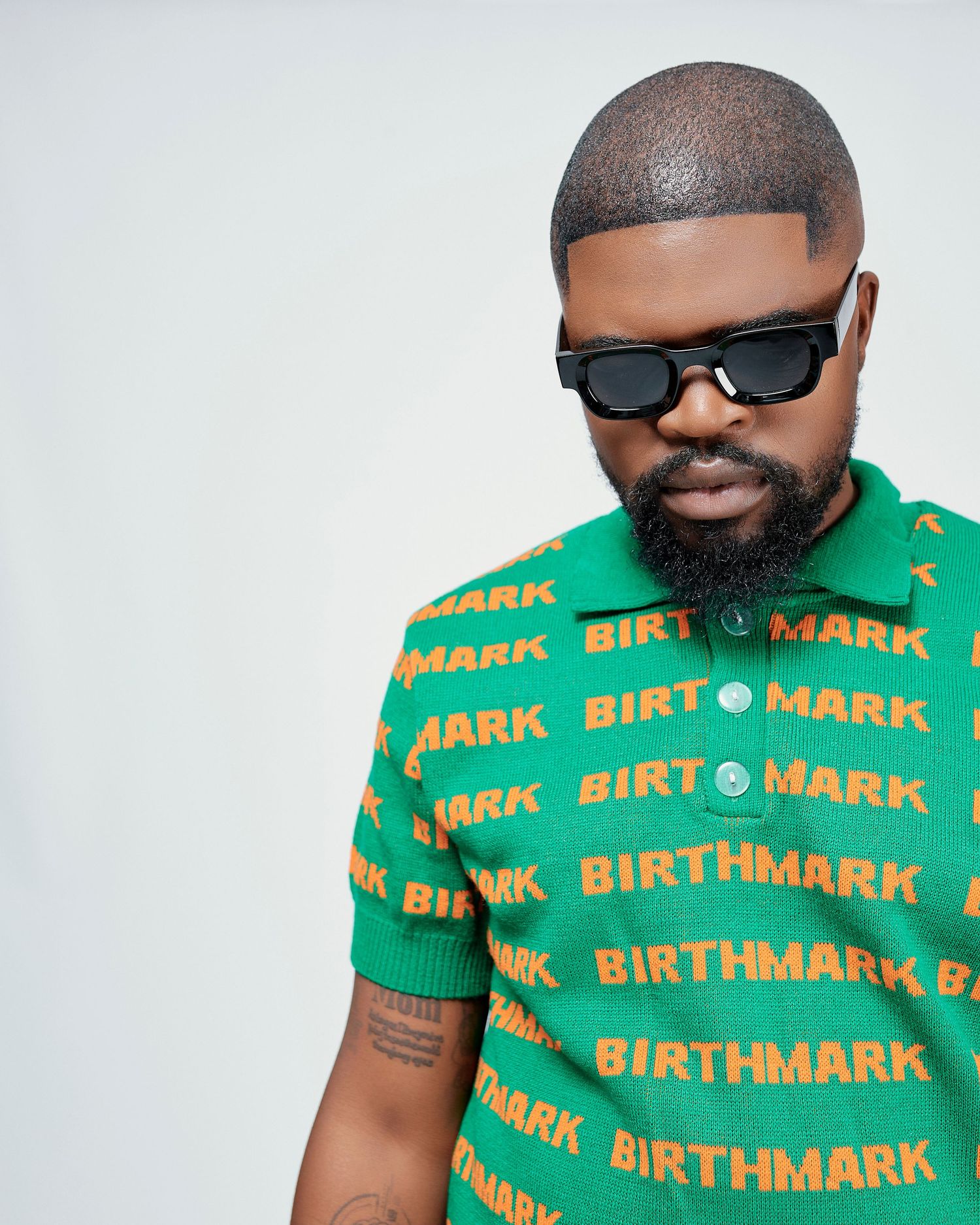 Bearded man in green Birthmark logo polo shirt wearing black sunglasses in studio setting.