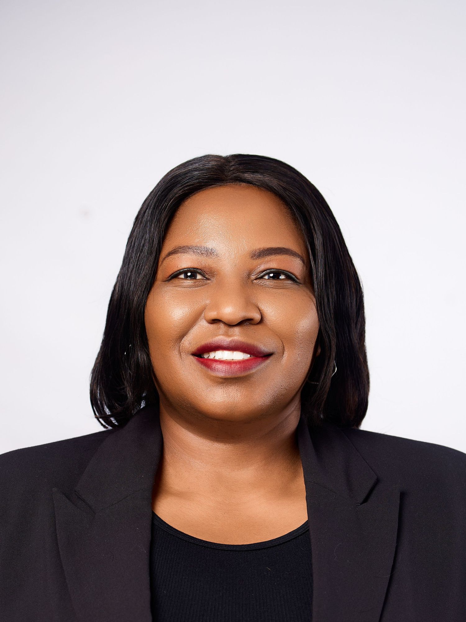 Professional headshot of a smiling woman with straight black hair in a black blazer against a gray background.