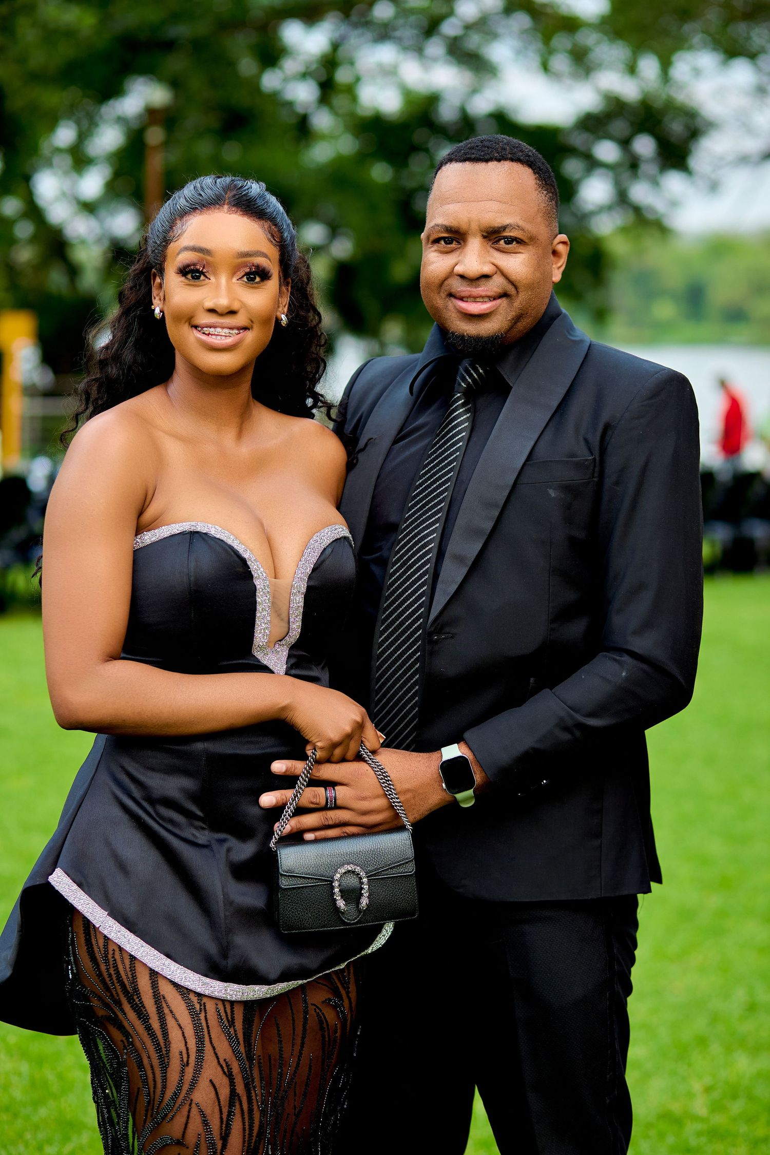 Stylish Black couple dressed in elegant black formal attire posing together at an outdoor event.