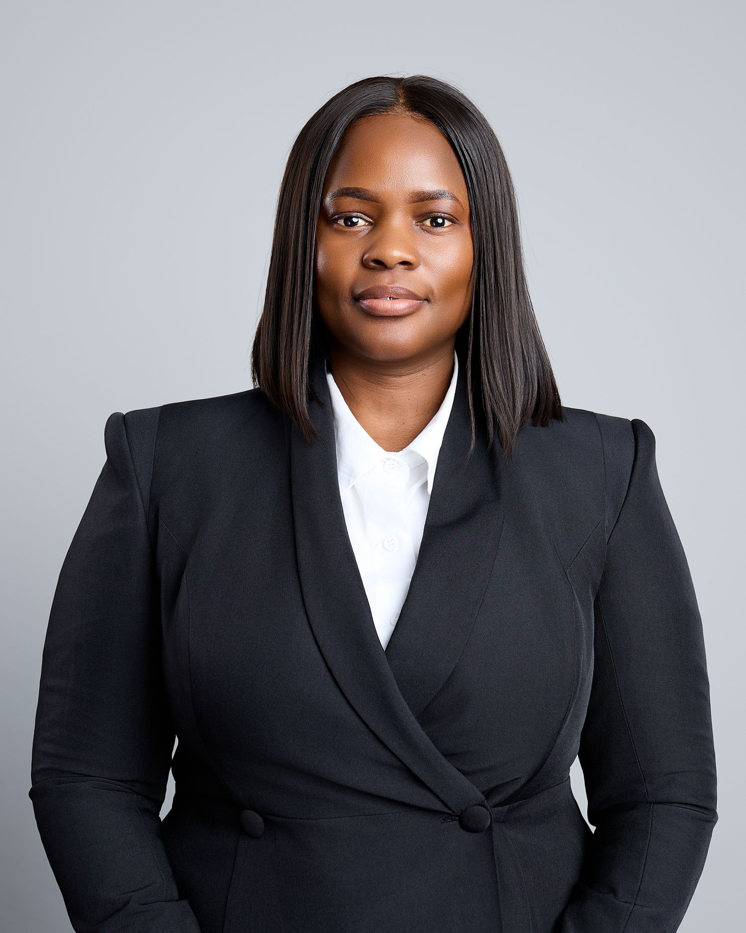 Professional Black woman in black blazer and white shirt poses for corporate headshot.