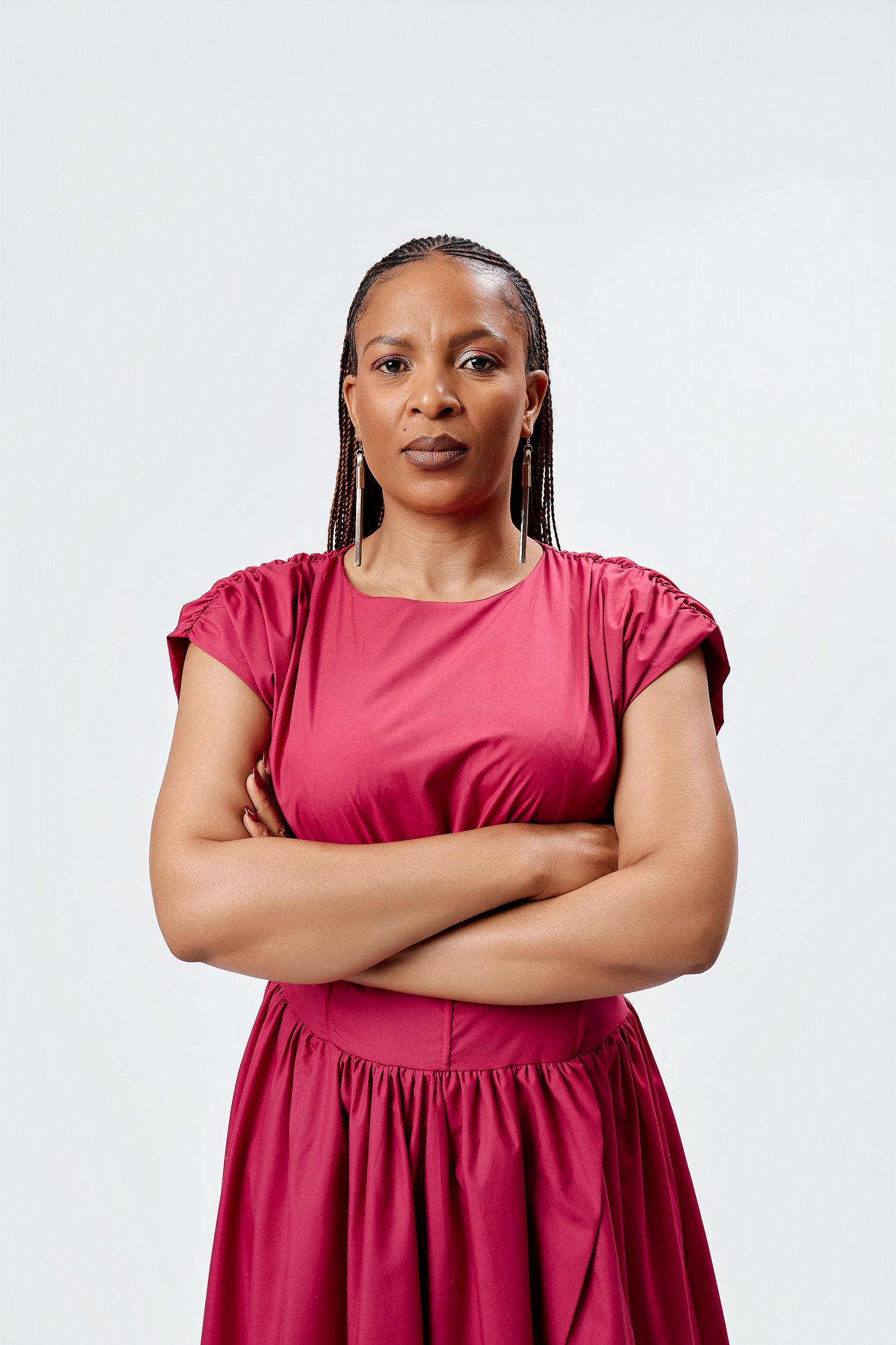 Confident Black woman in red dress stands with arms crossed for professional portrait photo.
