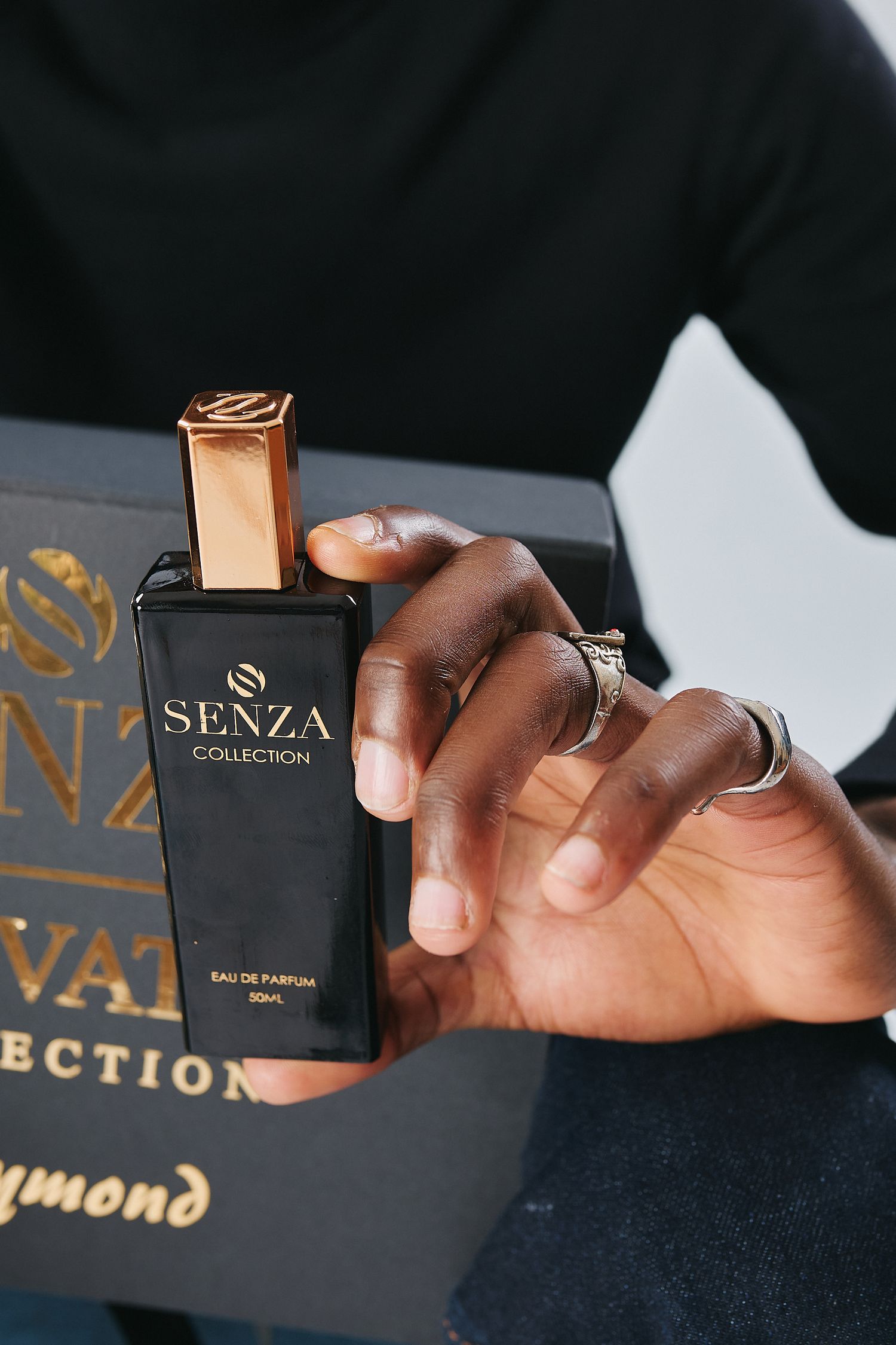 Close-up of hands holding Senza Collection Eau de Parfum bottle with black luxury gift box.
