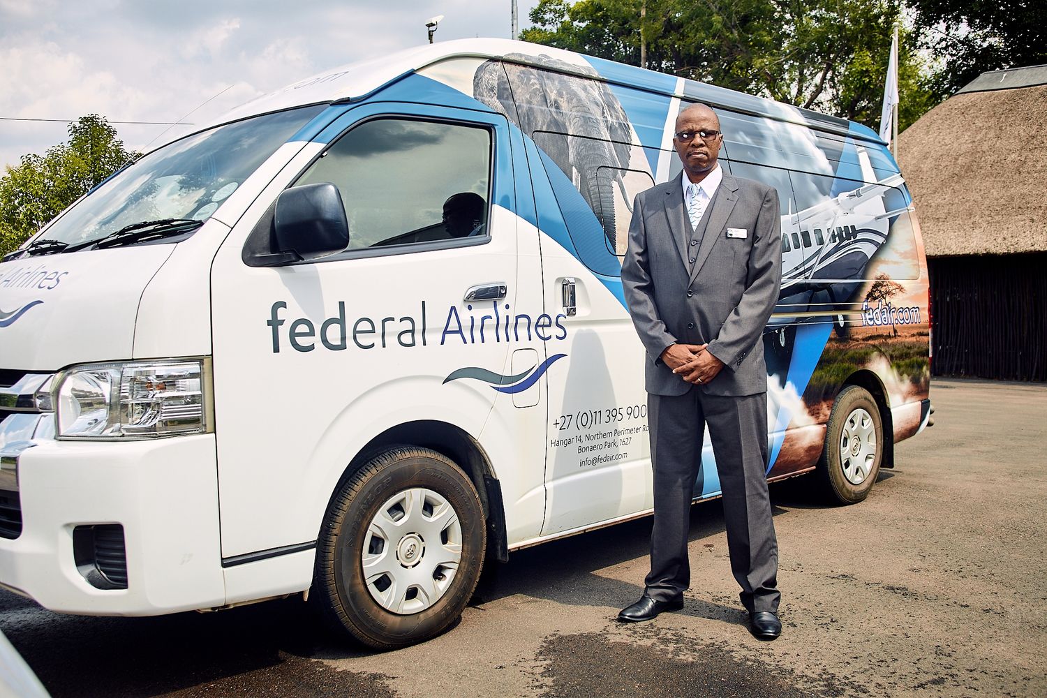 Male Federal Airlines employee in grey suit standing proudly beside a branded company van.