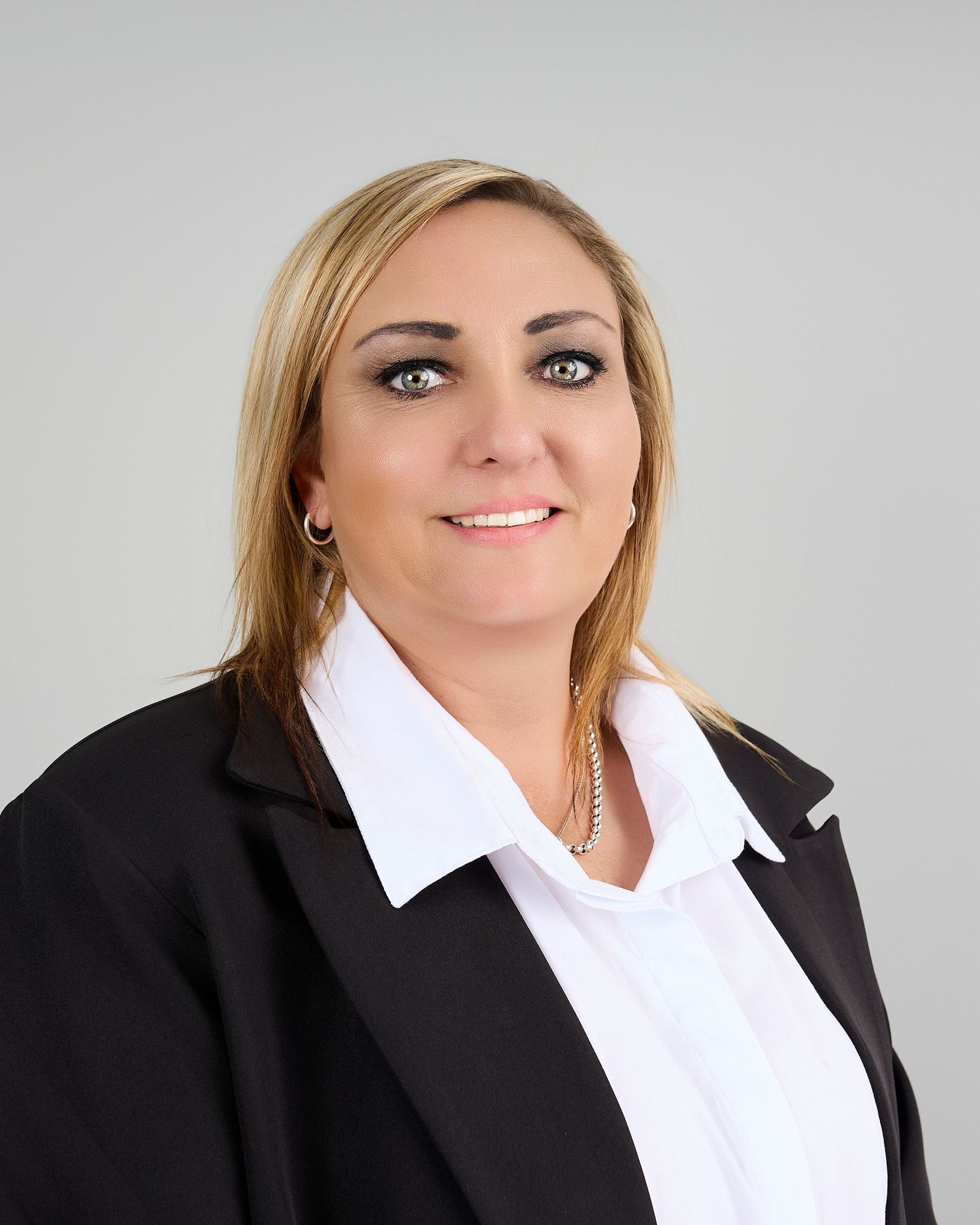 Smiling blonde woman in black blazer and white shirt poses for professional business headshot.