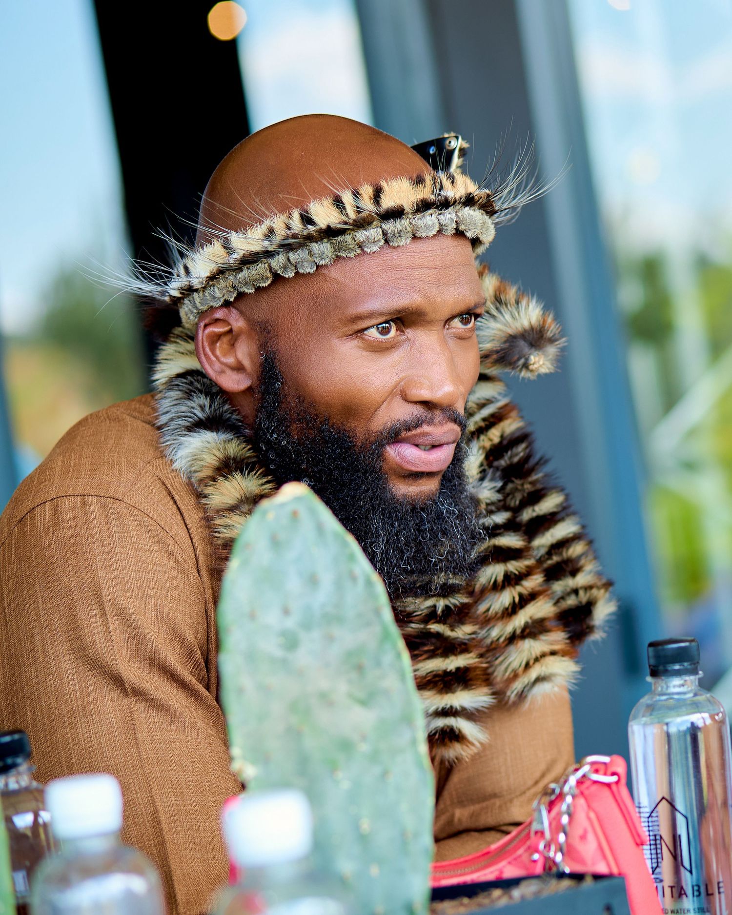 Man wearing traditional African leopard skin headdress and fur garment at outdoor gathering.