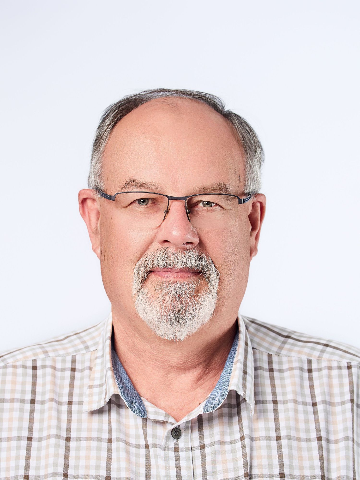 Older man with gray hair and goatee wearing rectangular glasses and plaid shirt against white background.