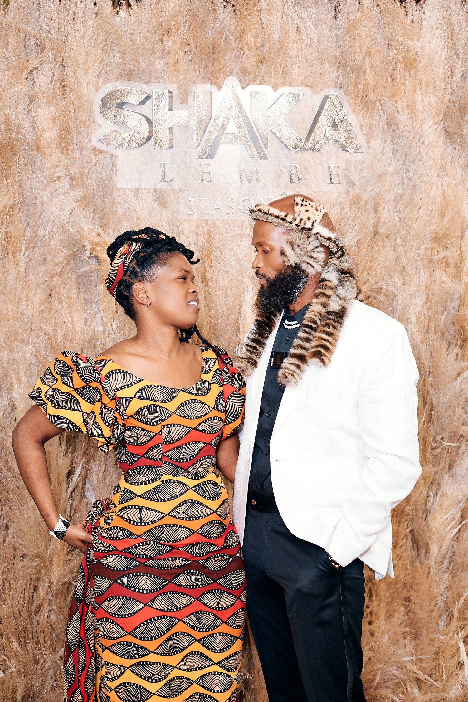Couple poses at Shaka Ilembe season premiere backdrop in traditional attire.