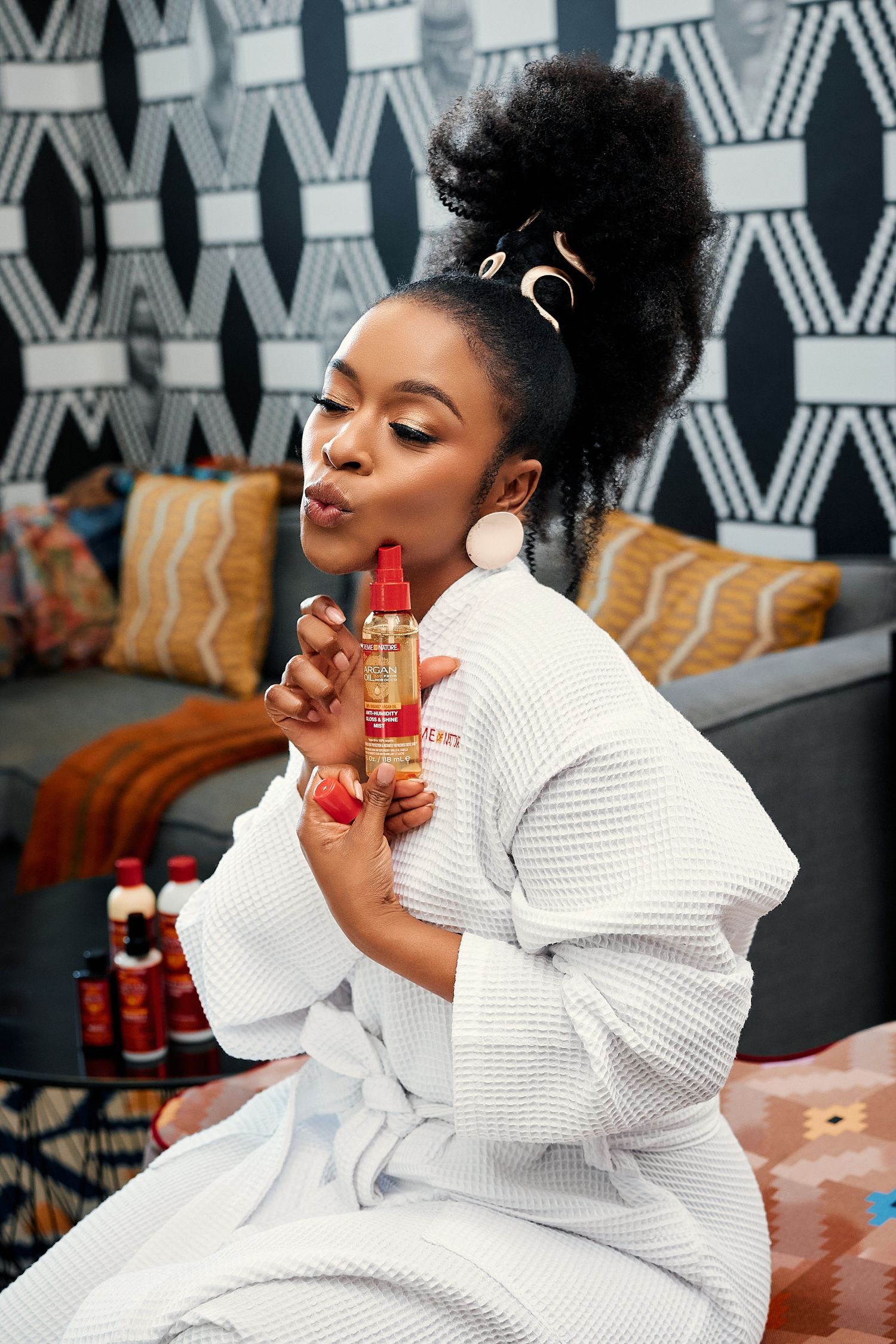 Black woman in white waffle robe poses playfully with Creme of Nature hair product bottle.