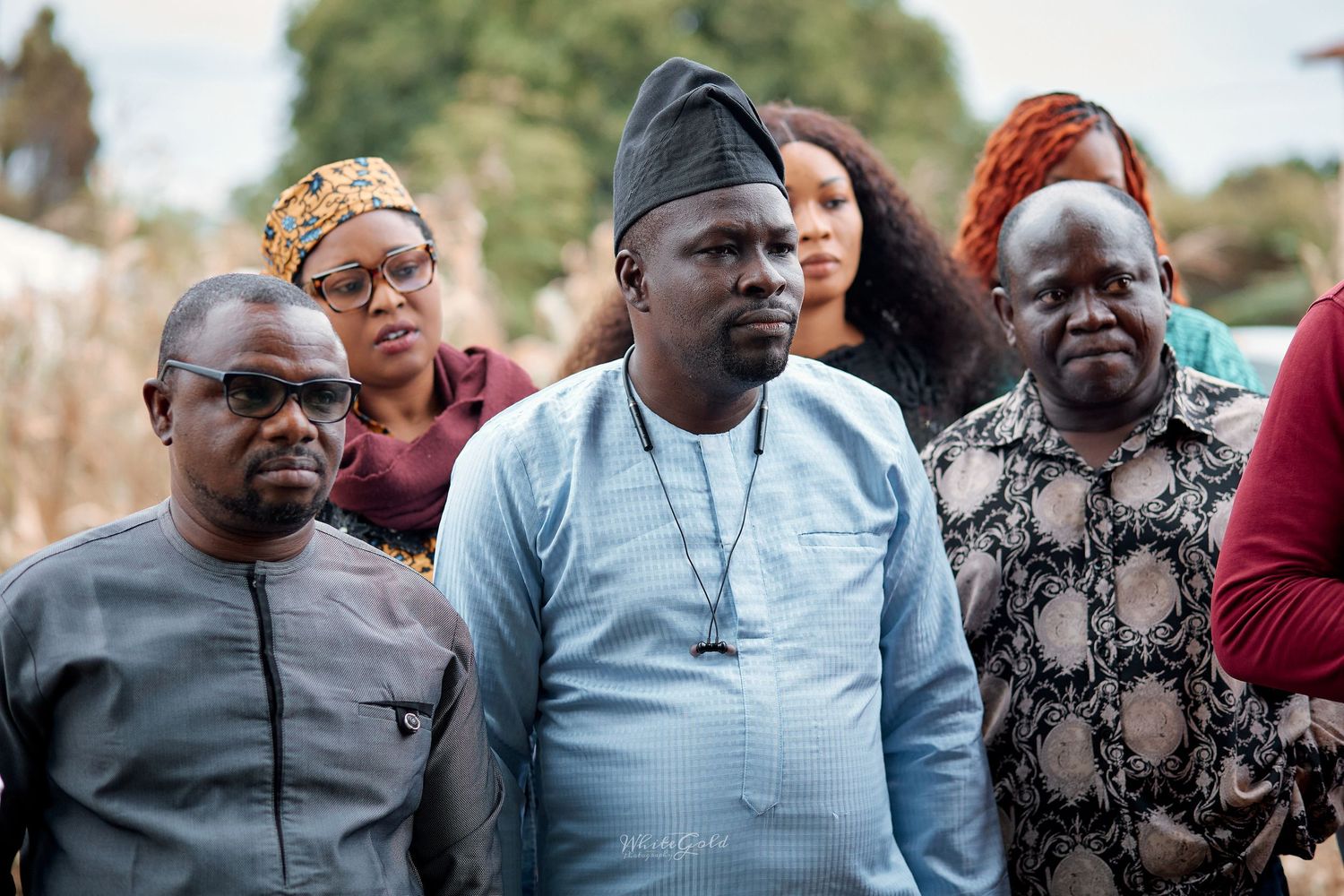 Group of men in traditional Nigerian attire stand together at outdoor event.