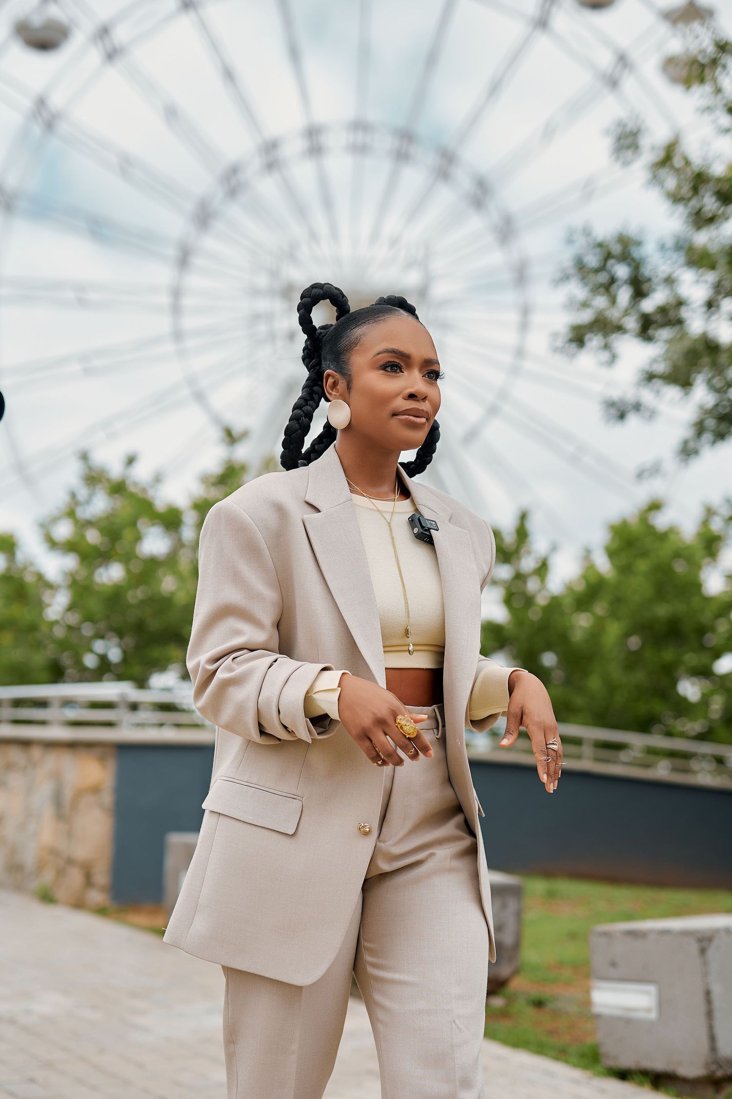 Stylish Black woman in beige suit with braided updo poses near Ferris wheel outdoors.