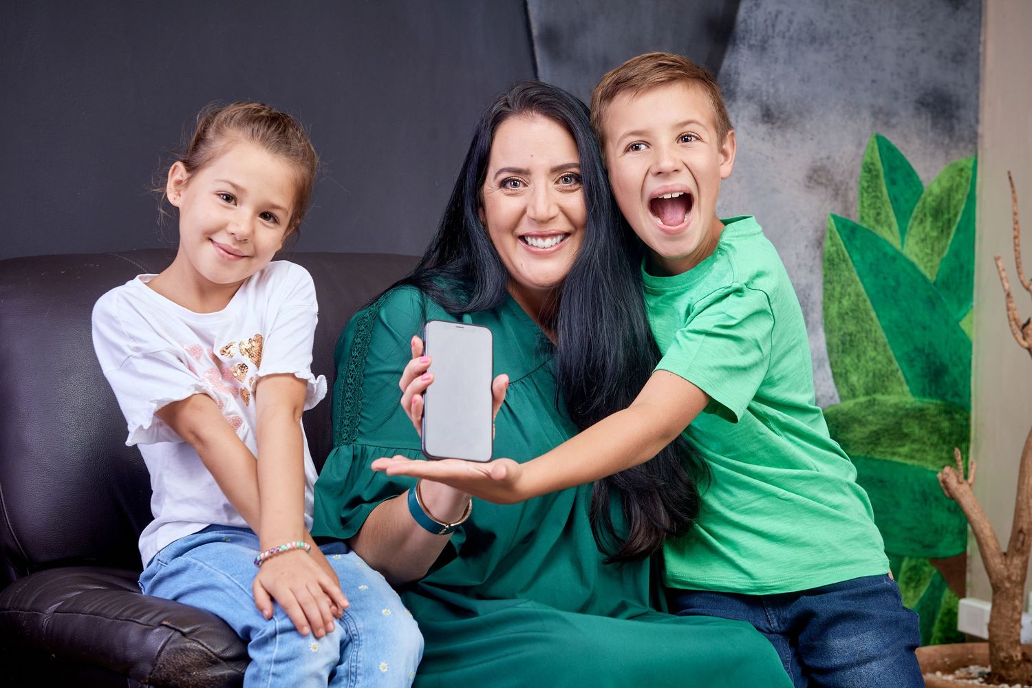 Happy mother and two excited children showing a smartphone with blank screen on a sofa.