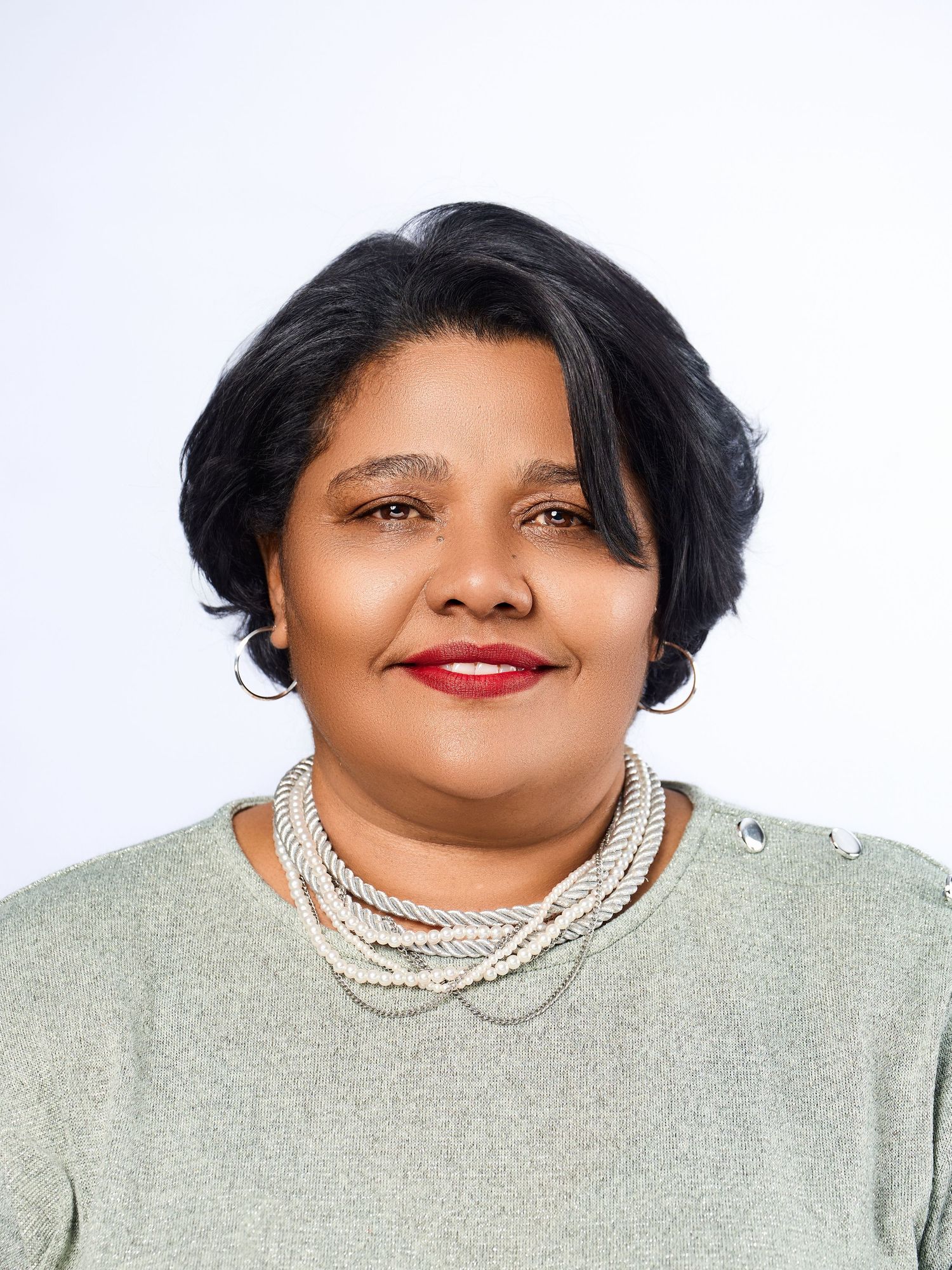 Professional headshot of a woman with short black hair wearing a pearl necklace and sage green top.