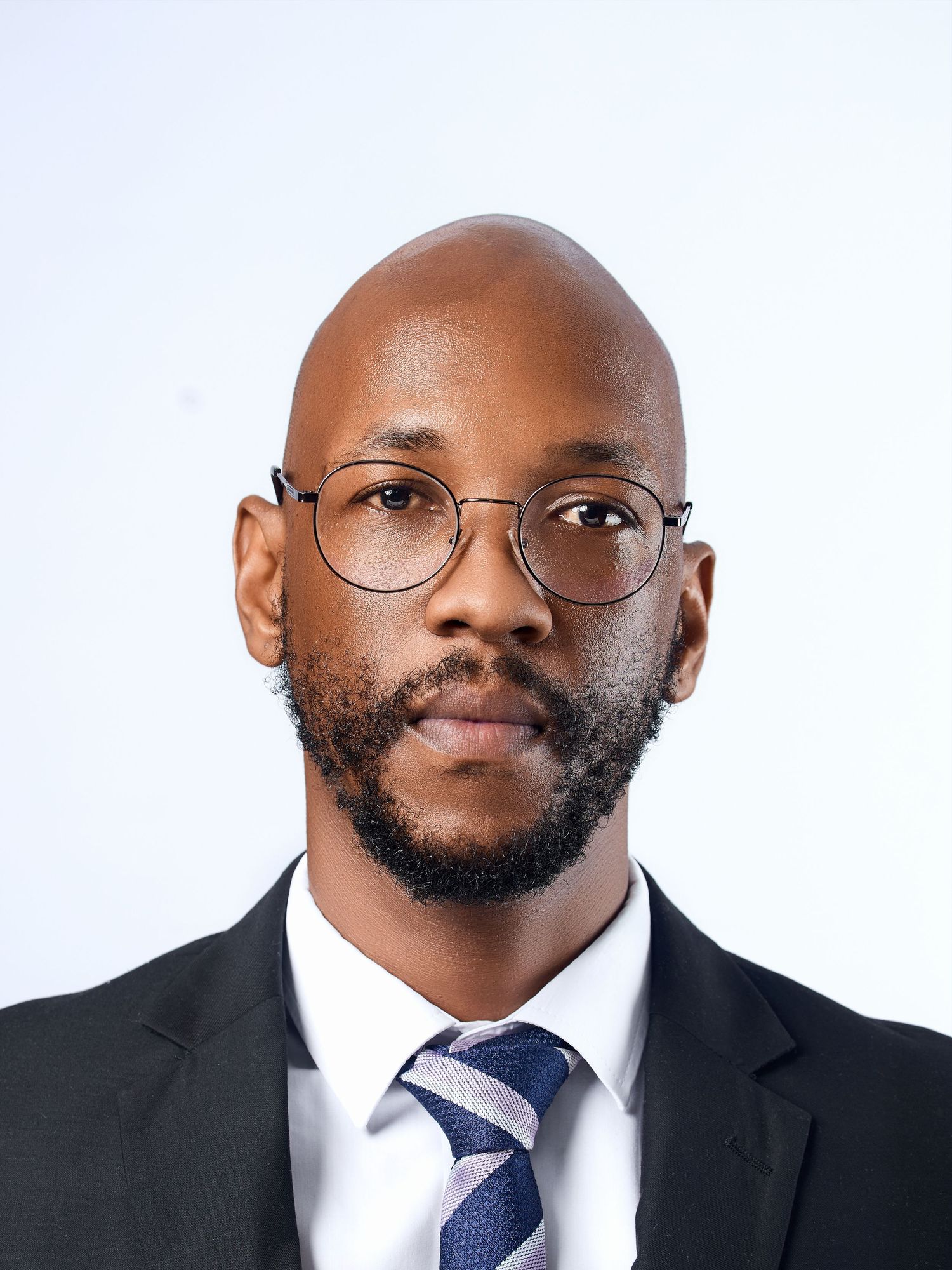 Professional headshot of a bald Black man with a beard wearing glasses and a dark suit with a blue tie.