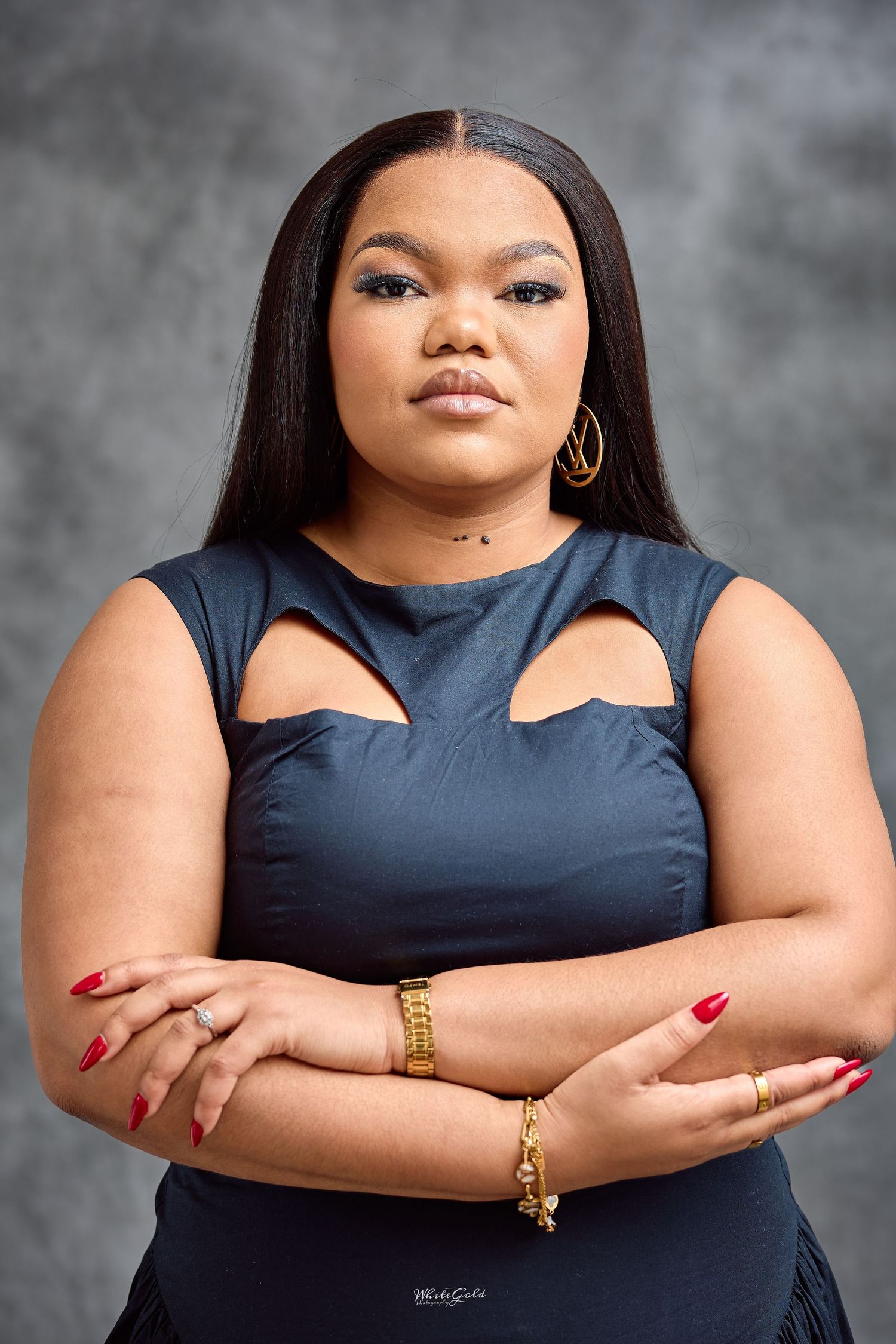 Confident plus-size woman in navy cutout dress stands with arms crossed for professional portrait.