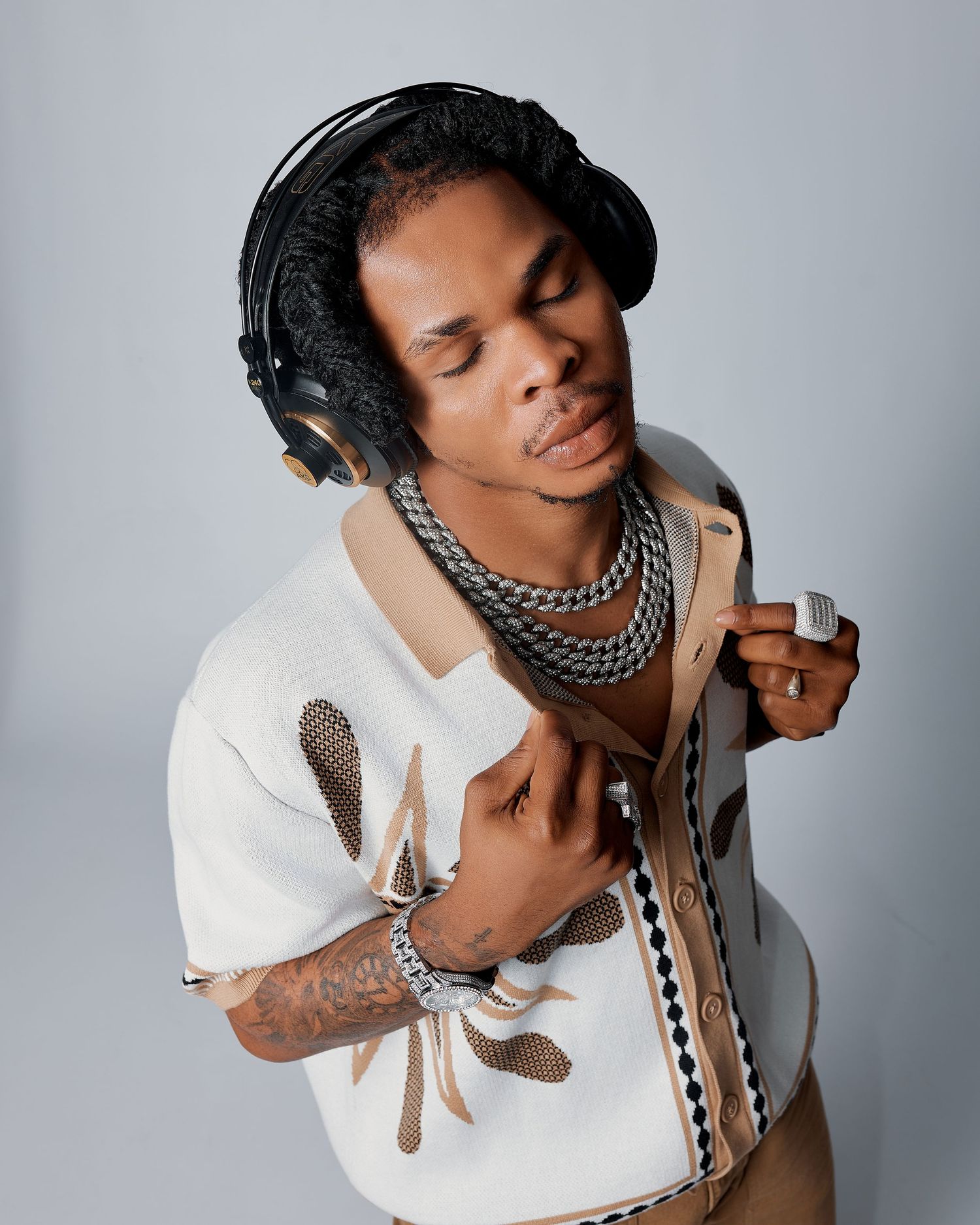 Young male musician wearing headphones and silver chain necklaces in a white patterned shirt.