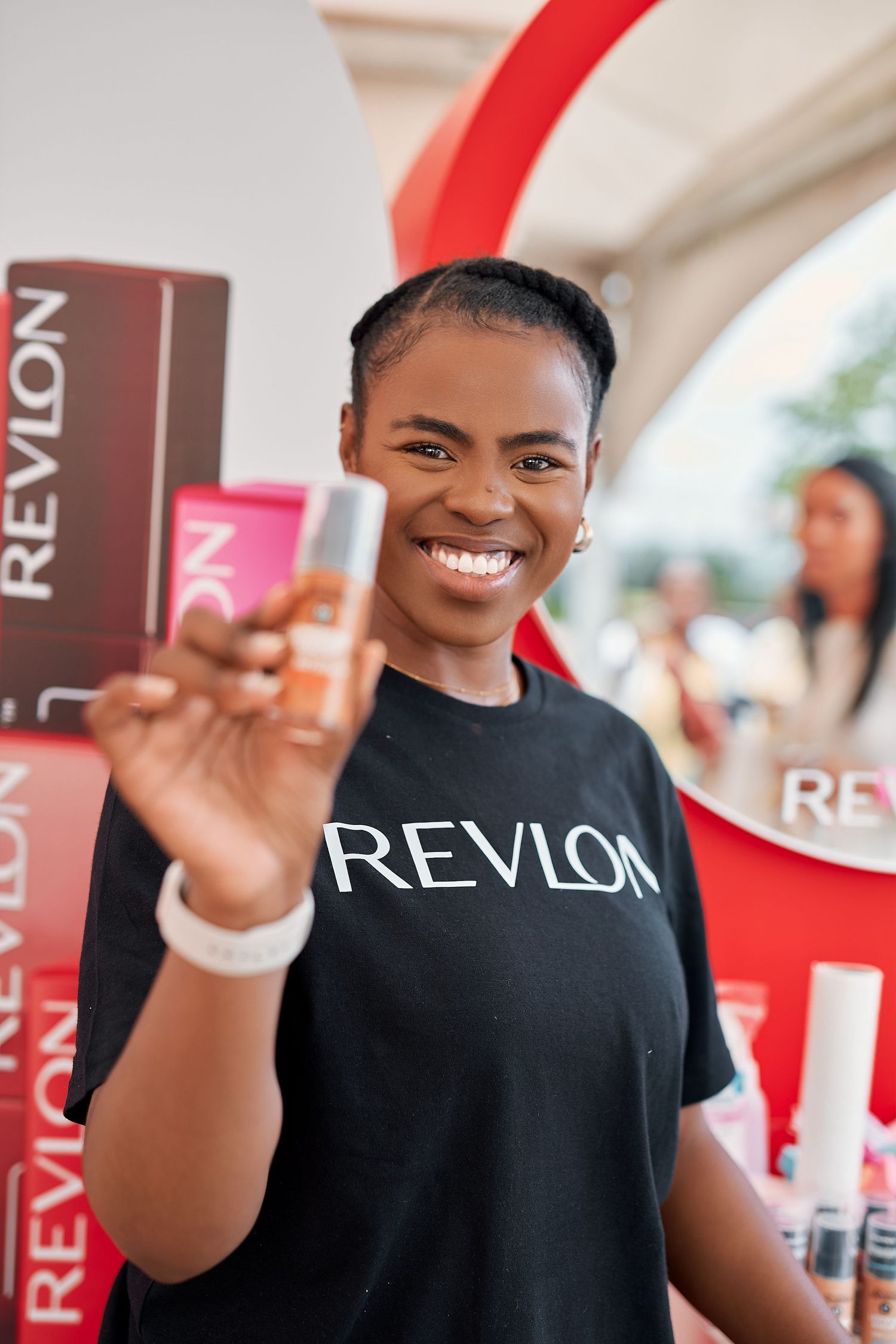 Smiling woman in Revlon t-shirt holding up a foundation product at a Revlon brand event.
