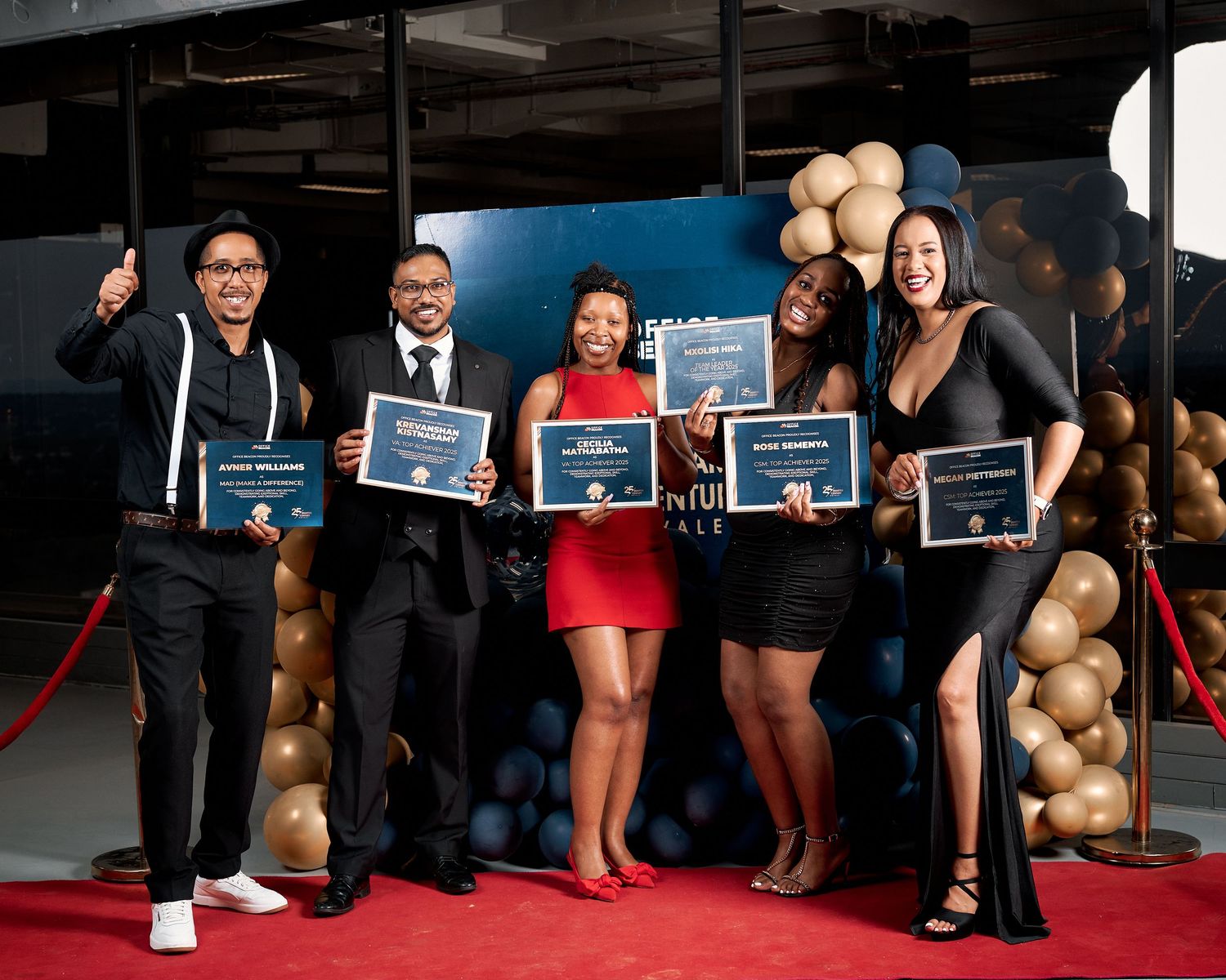 Five people proudly holding certificates on a red carpet at an awards recognition ceremony.