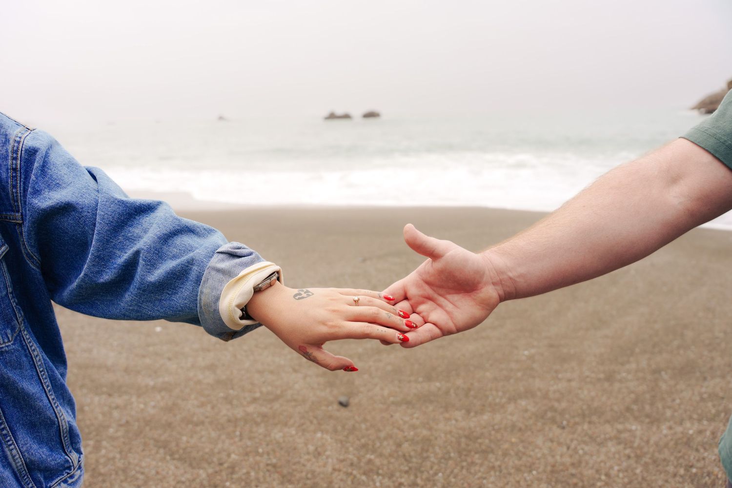 A couple holding hands during their engagement photography session at Duncan's Landing overlook beach in Bodega bay.