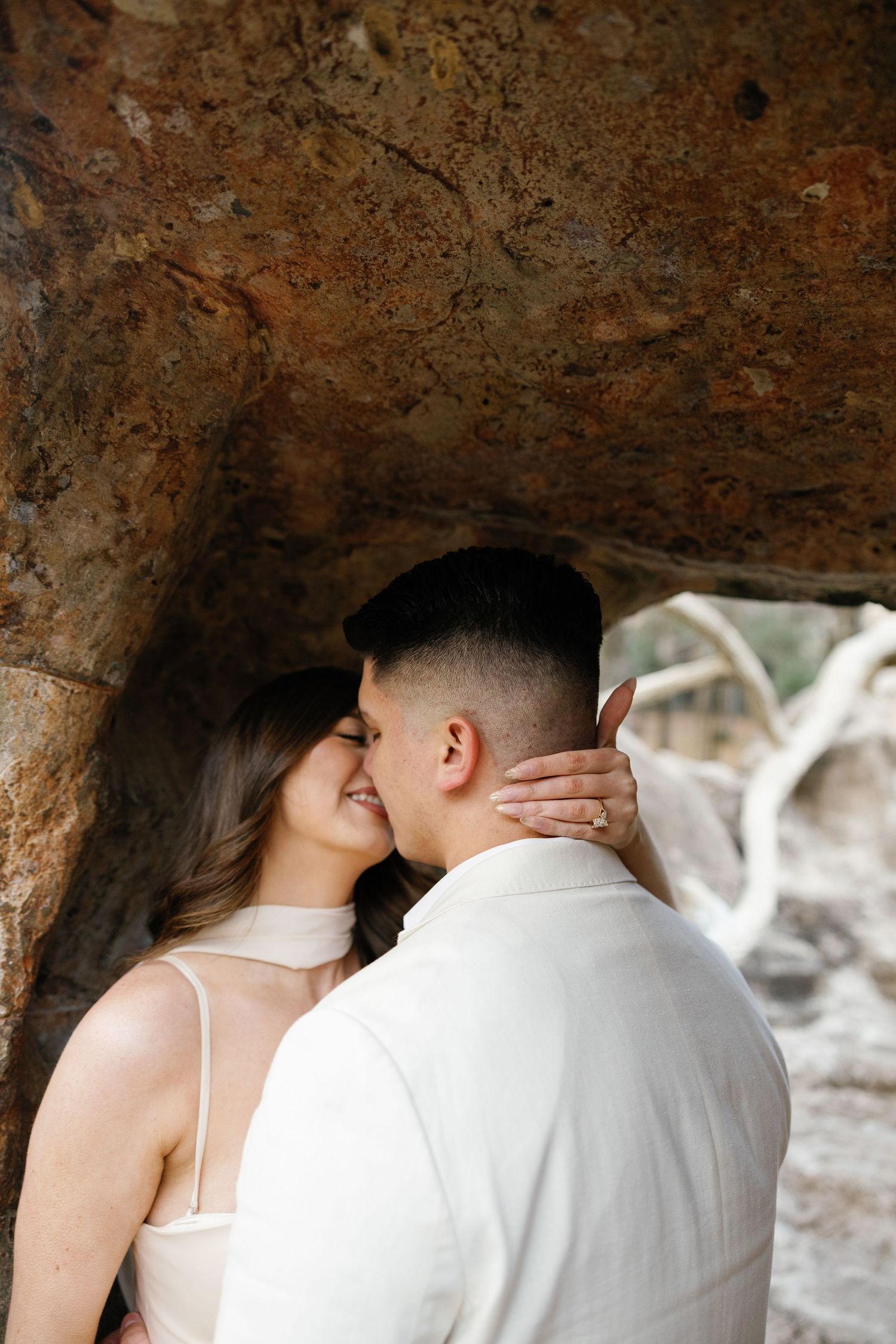 Couple sharing a romantic moment under a rocky overhang, woman smiling with hand on mans neck.