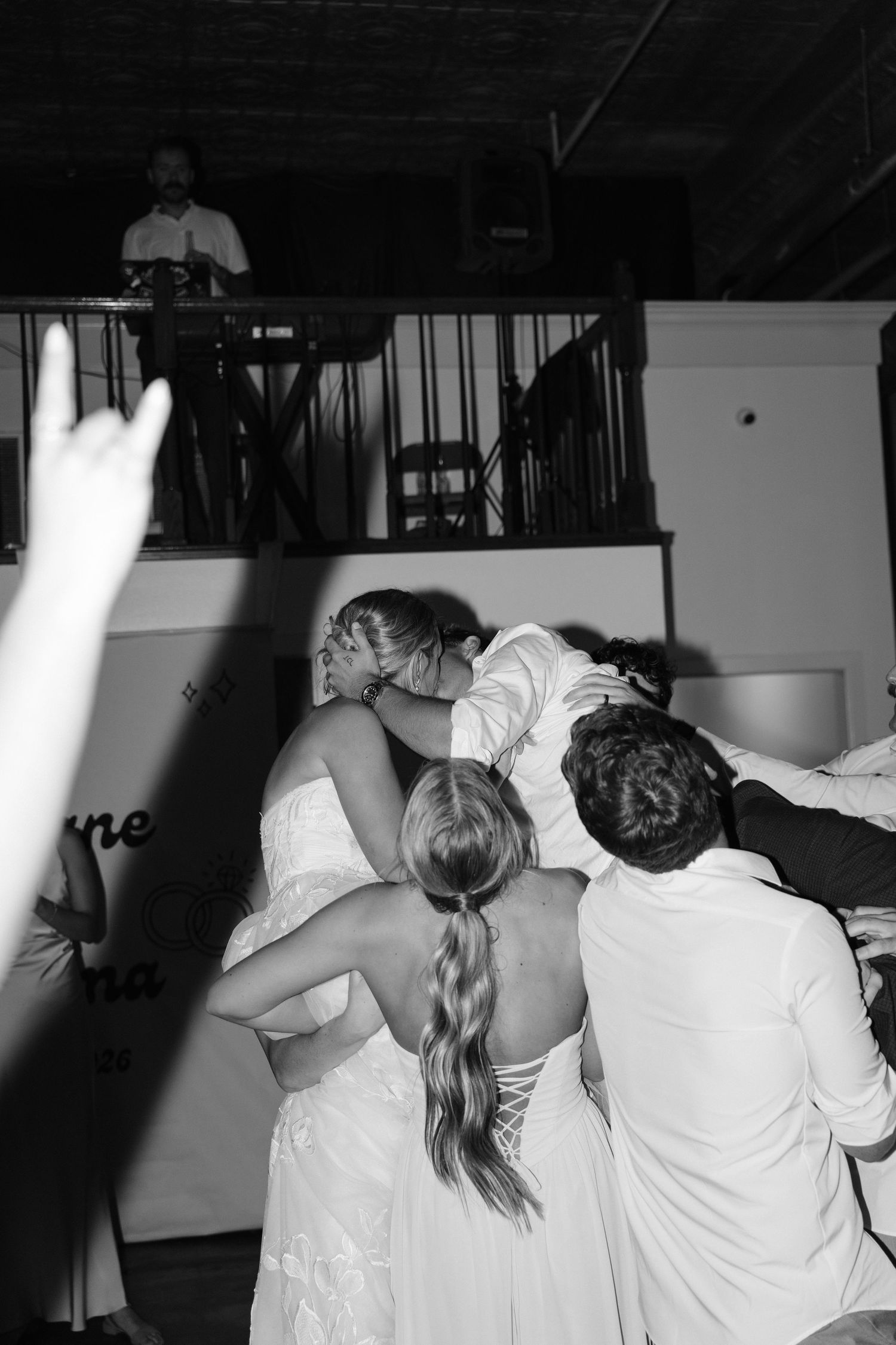 Black and white photo of bride and groom sharing a kiss surrounded by guests at lively wedding reception.