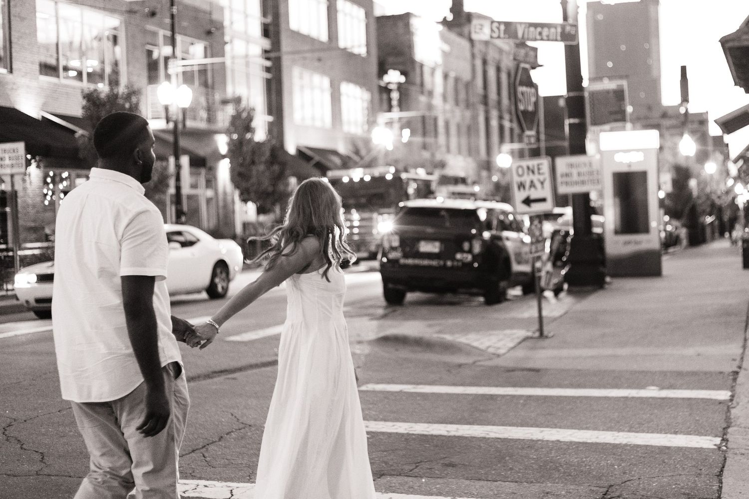 Couple holding hands while crossing a city street at night in black and white photo.